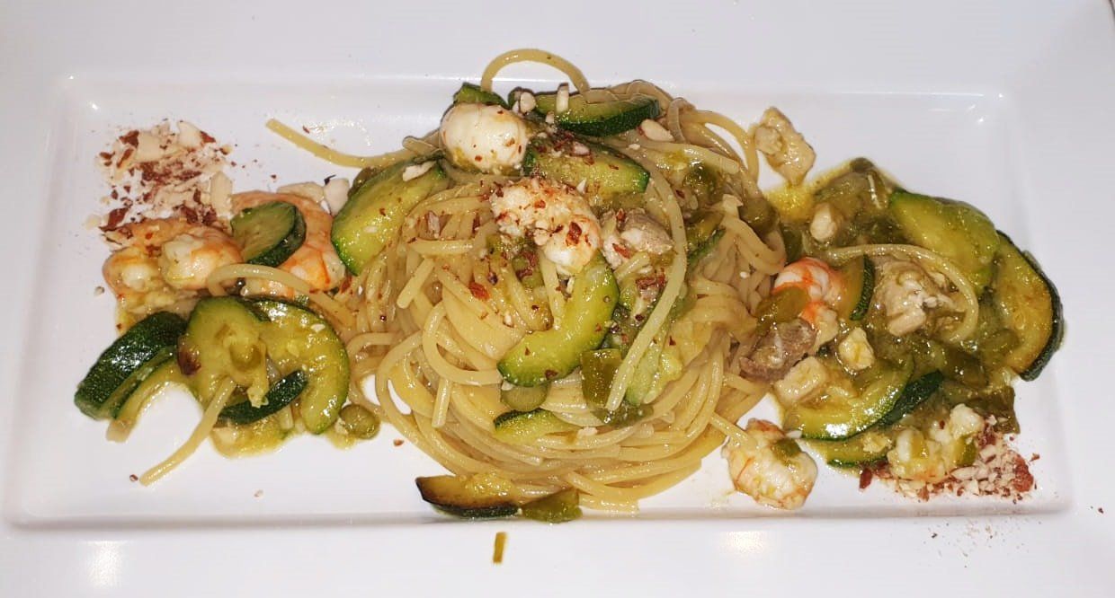 Piatto di spaghetti con zucchine e gamberi su un piatto bianco rettangolare, cosparso di fiocchi di peperoncino rosso.