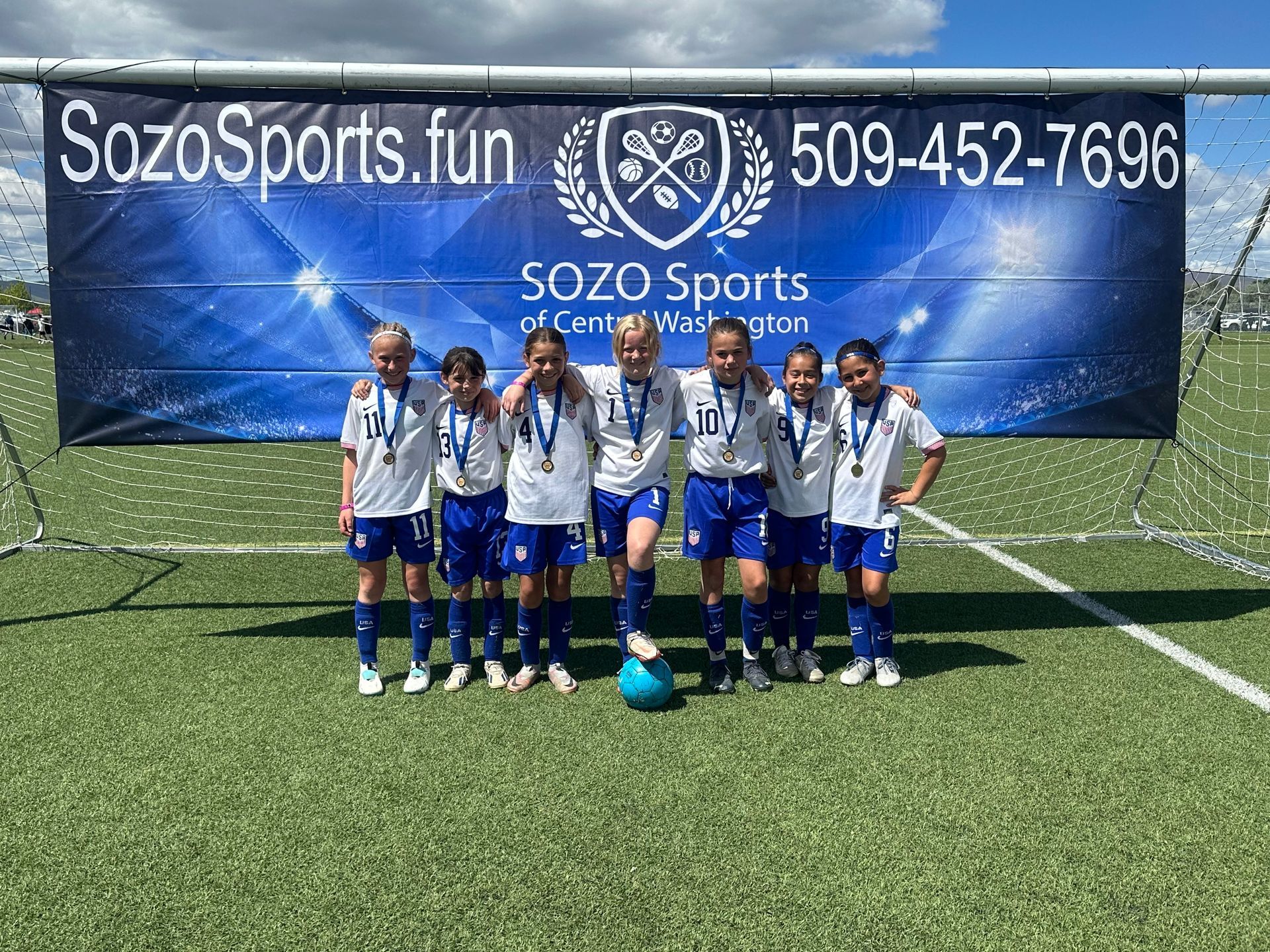 A group of young girls are posing for a picture on a soccer field.