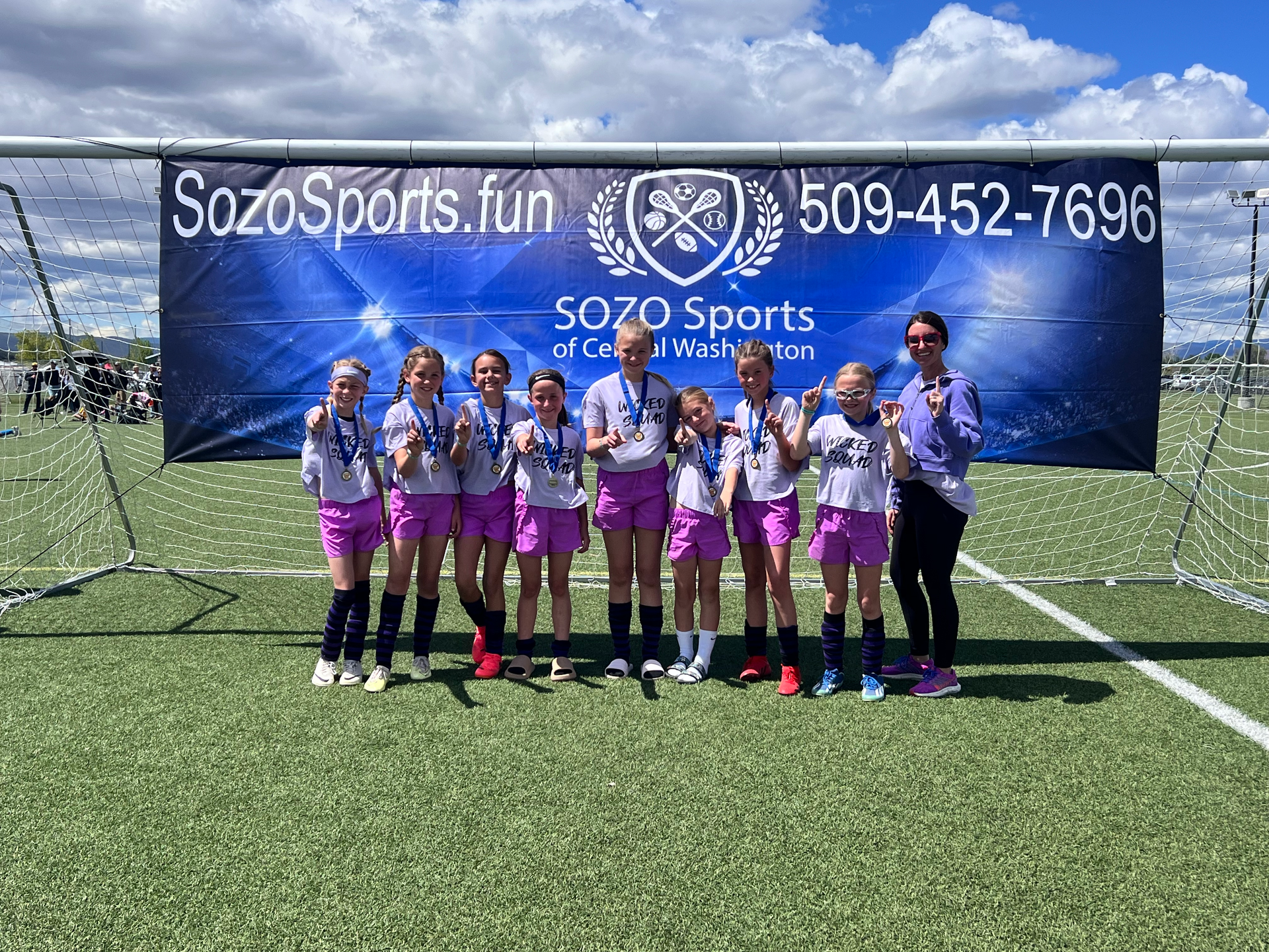 A group of young girls are posing for a picture on a soccer field.