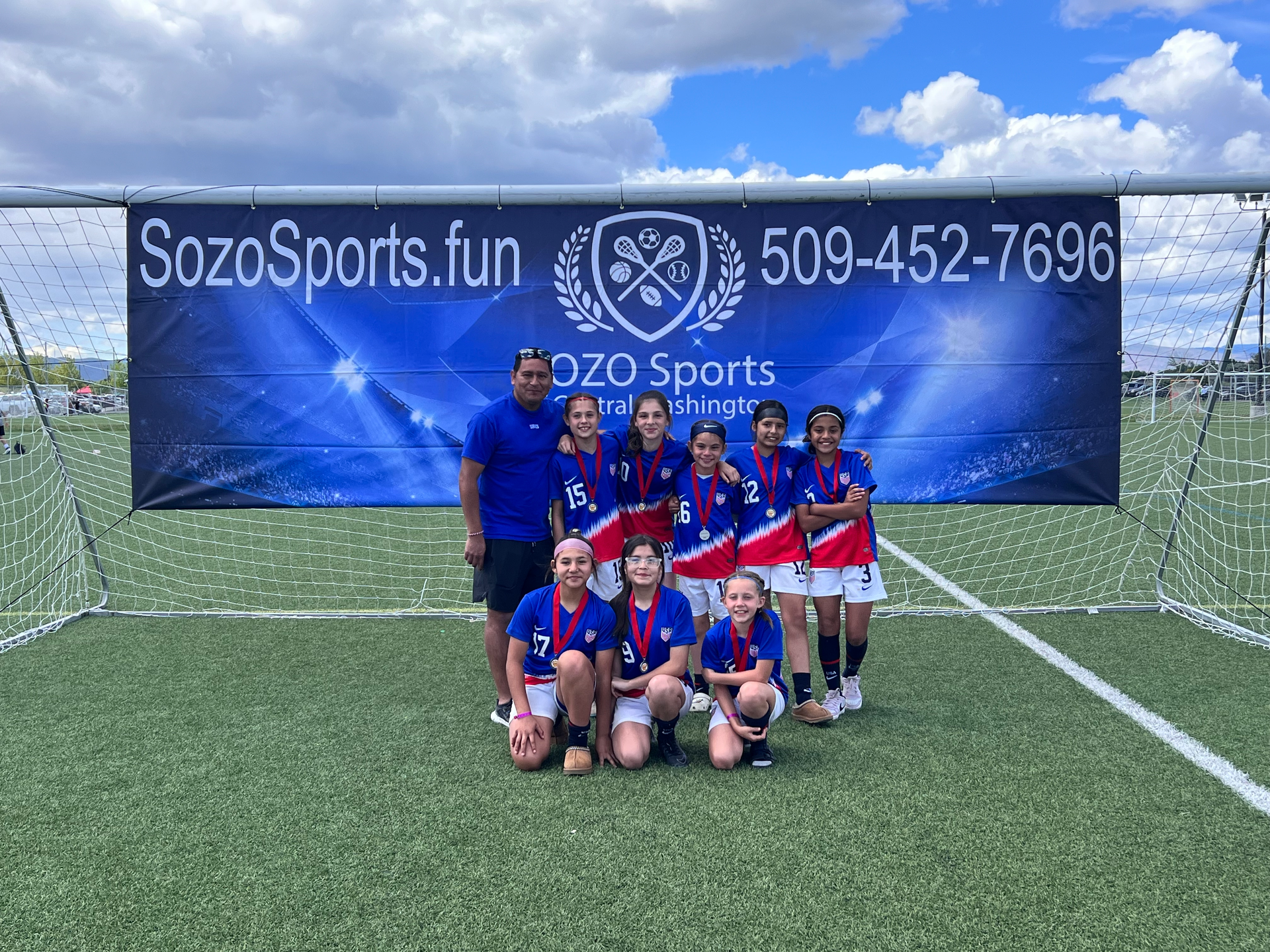 A group of young girls are posing for a picture on a soccer field.