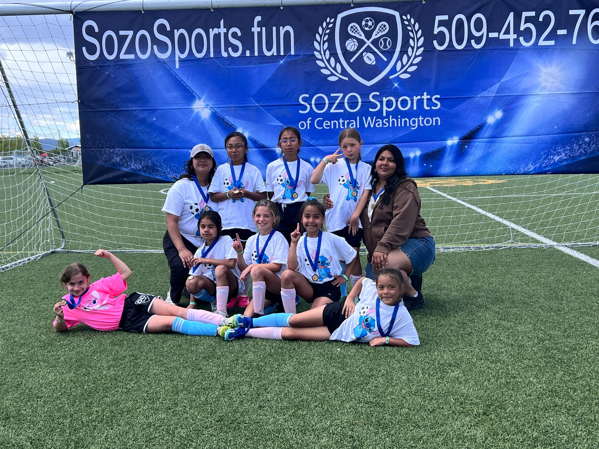A group of young girls are posing for a picture on a soccer field.