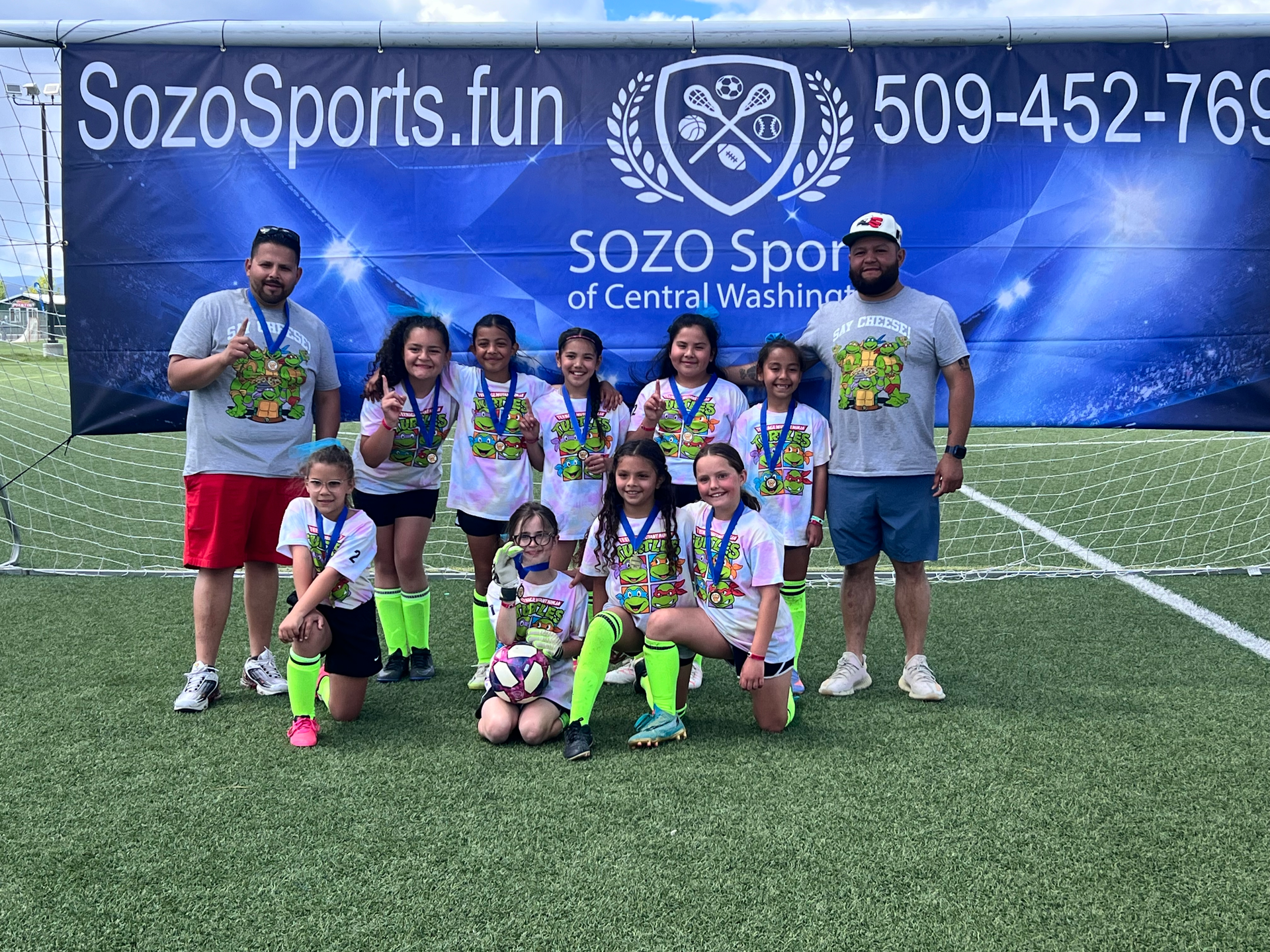 A group of young girls are posing for a picture on a soccer field.