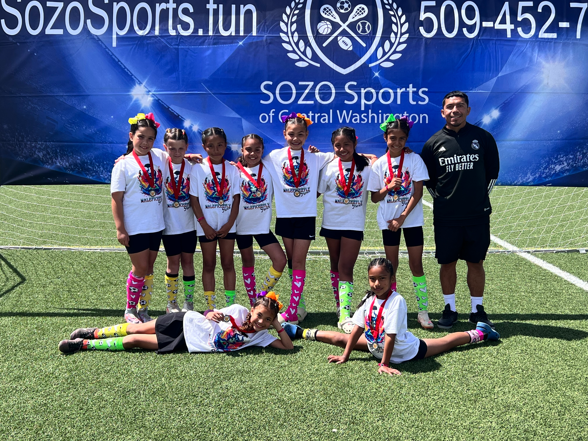 A group of young girls are posing for a picture on a soccer field.