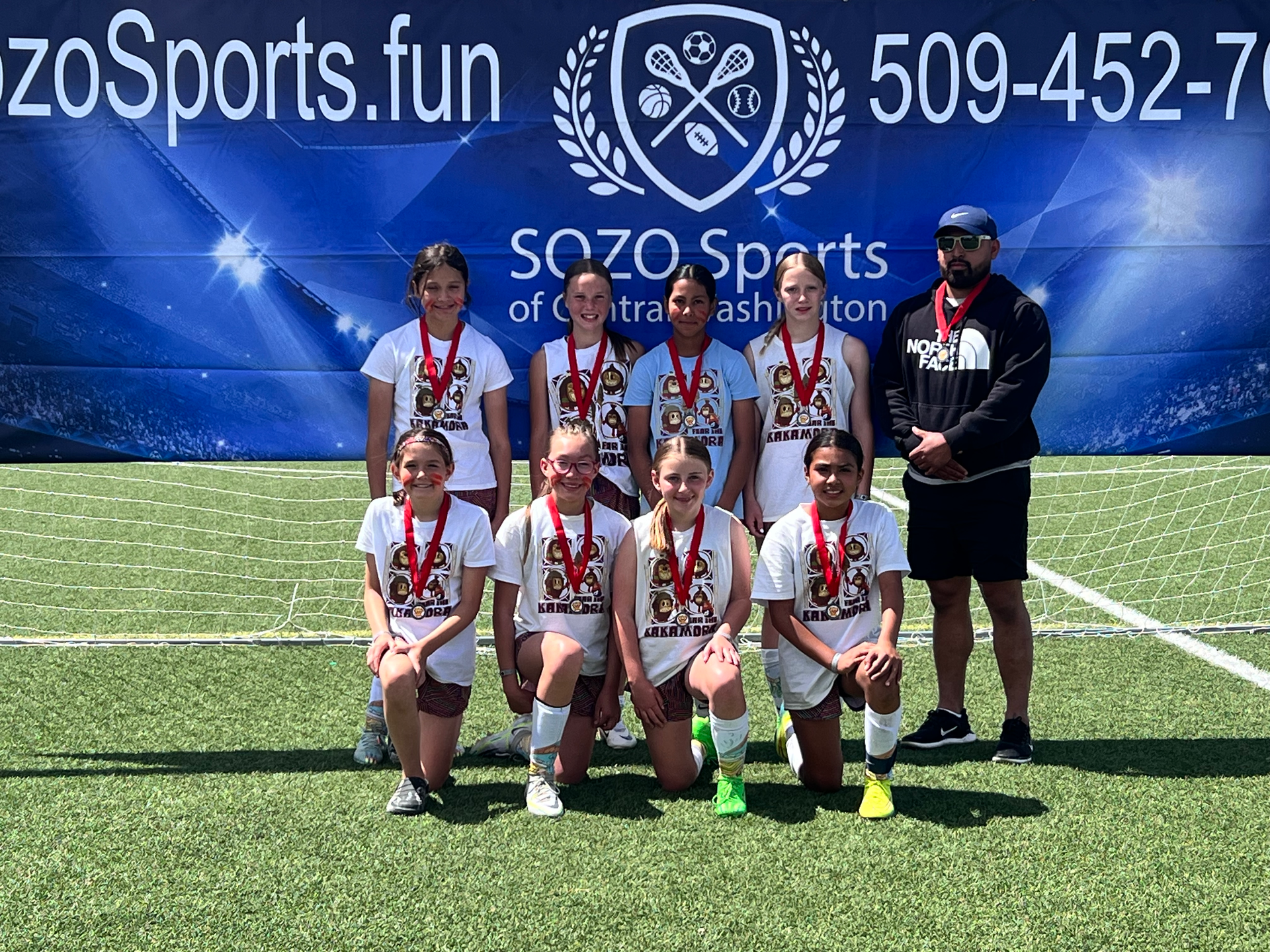 A group of young girls are posing for a picture on a soccer field.