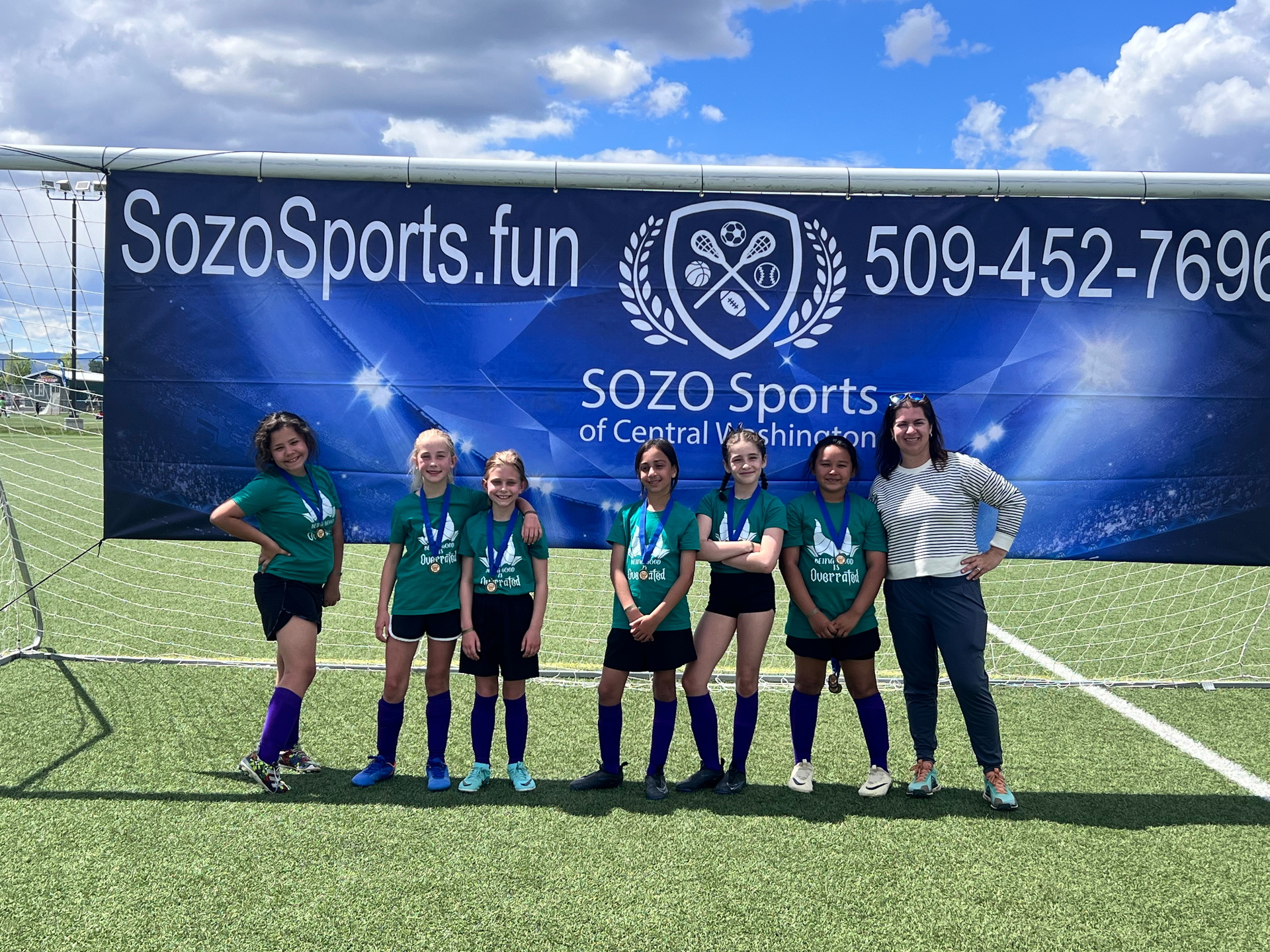 A group of young girls are posing for a picture on a soccer field.
