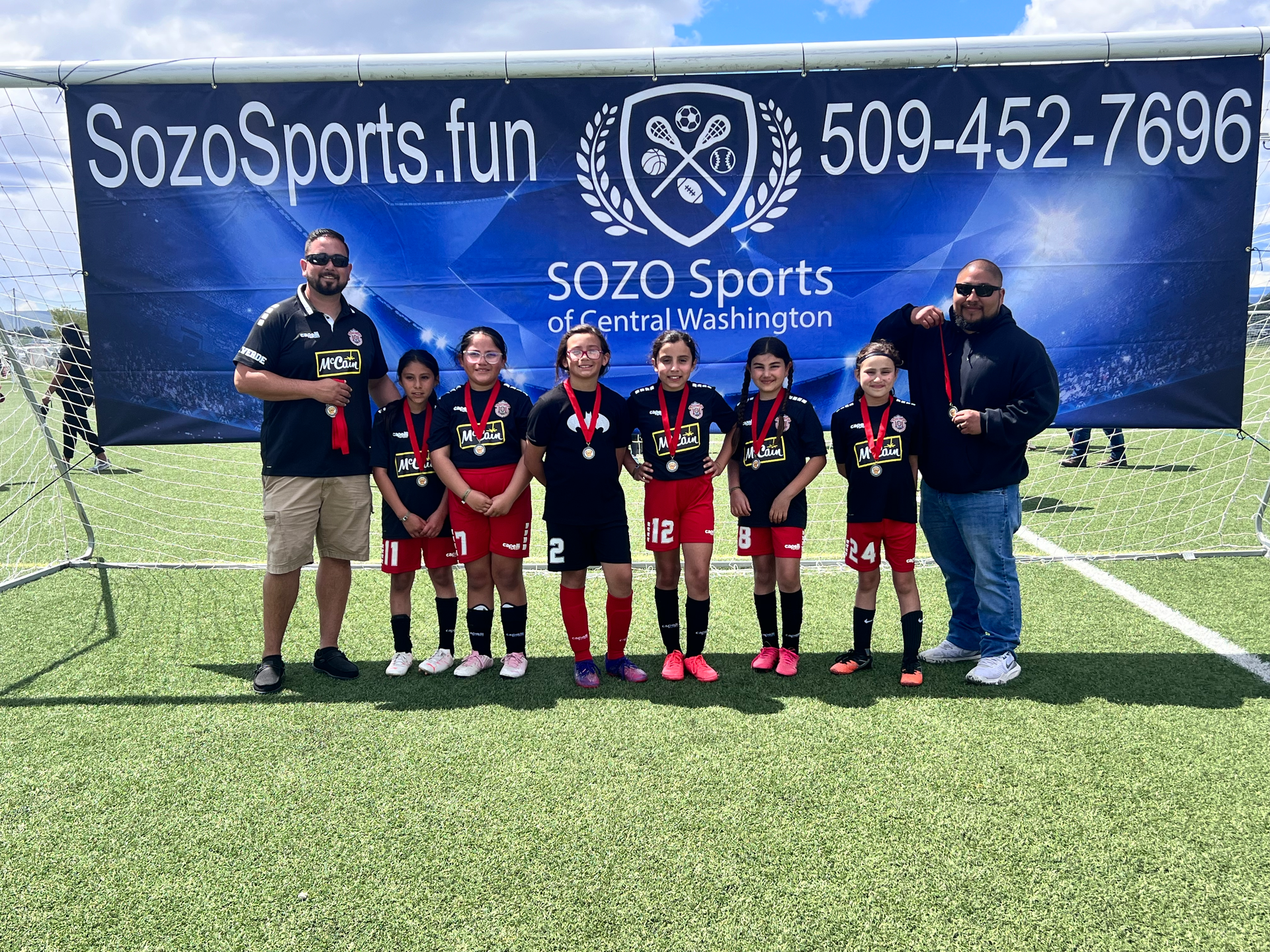 A group of young girls are posing for a picture on a soccer field.
