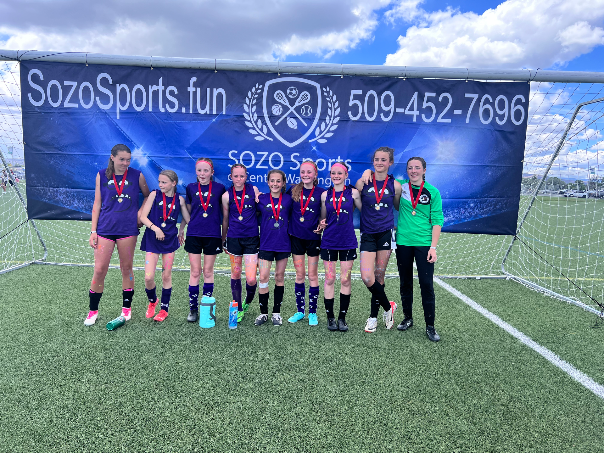 A group of young girls are posing for a picture on a soccer field.