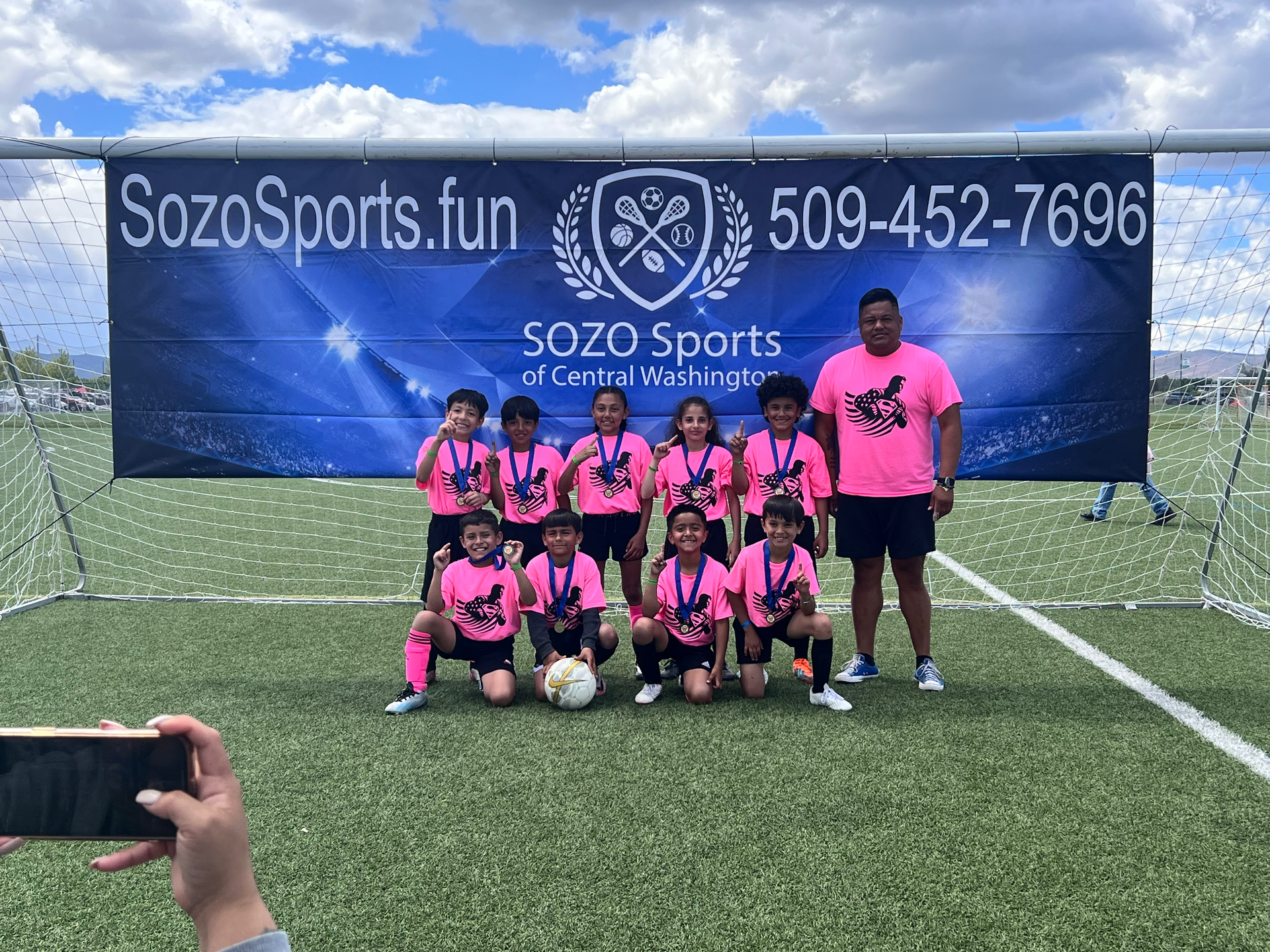 A group of young kids are posing for a picture on a soccer field.
