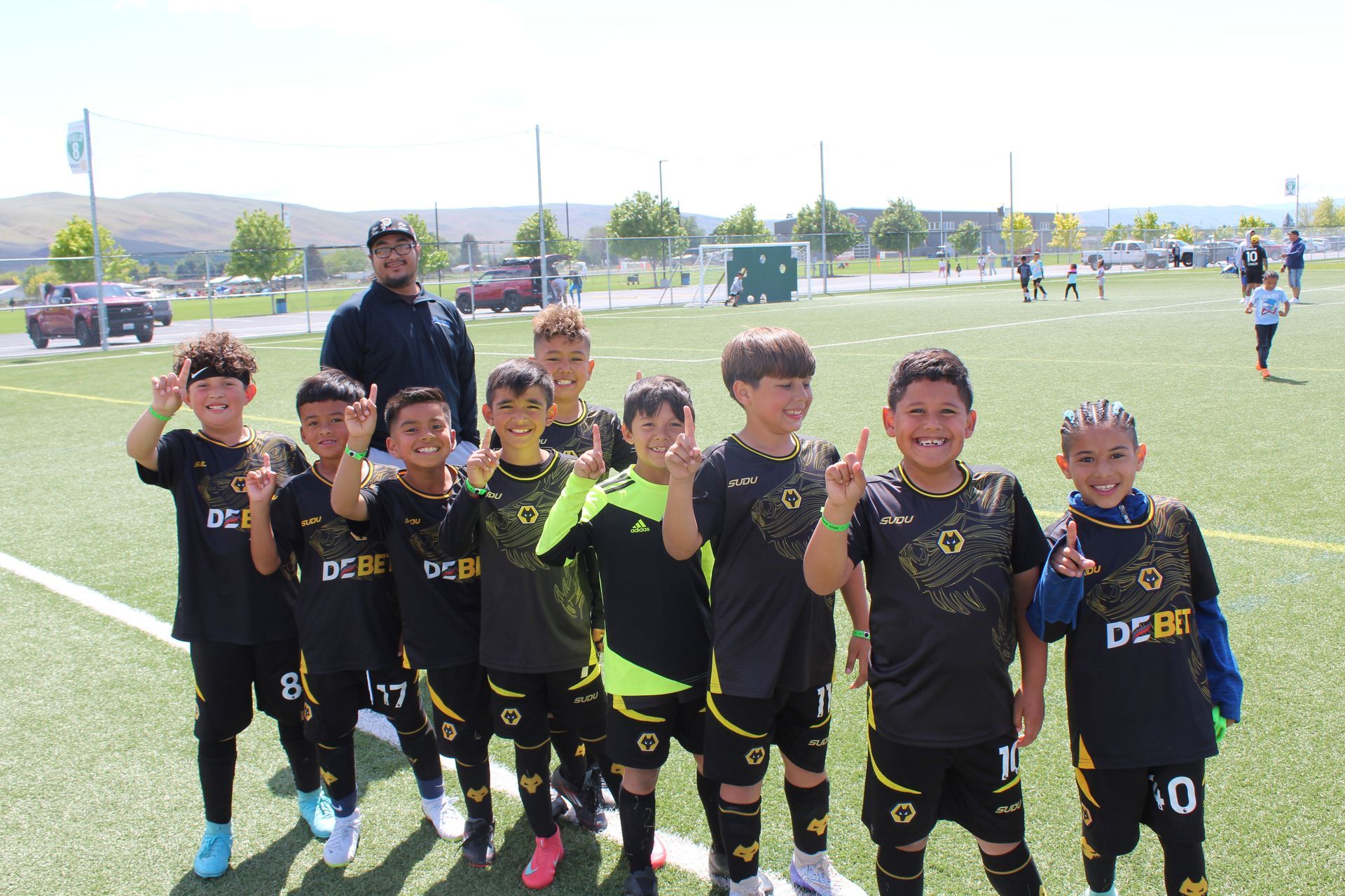 A soccer team in black and yellow uniforms posing for a photo on a sunny field with their coach behind them.