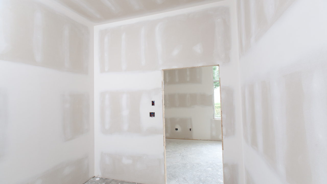 Unfinished drywall interior with a doorway into a bright room and a small window.