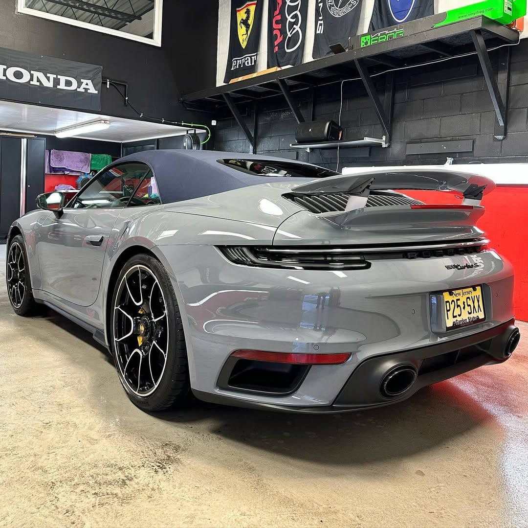 A gray porsche 911 turbo s convertible is parked in a garage.