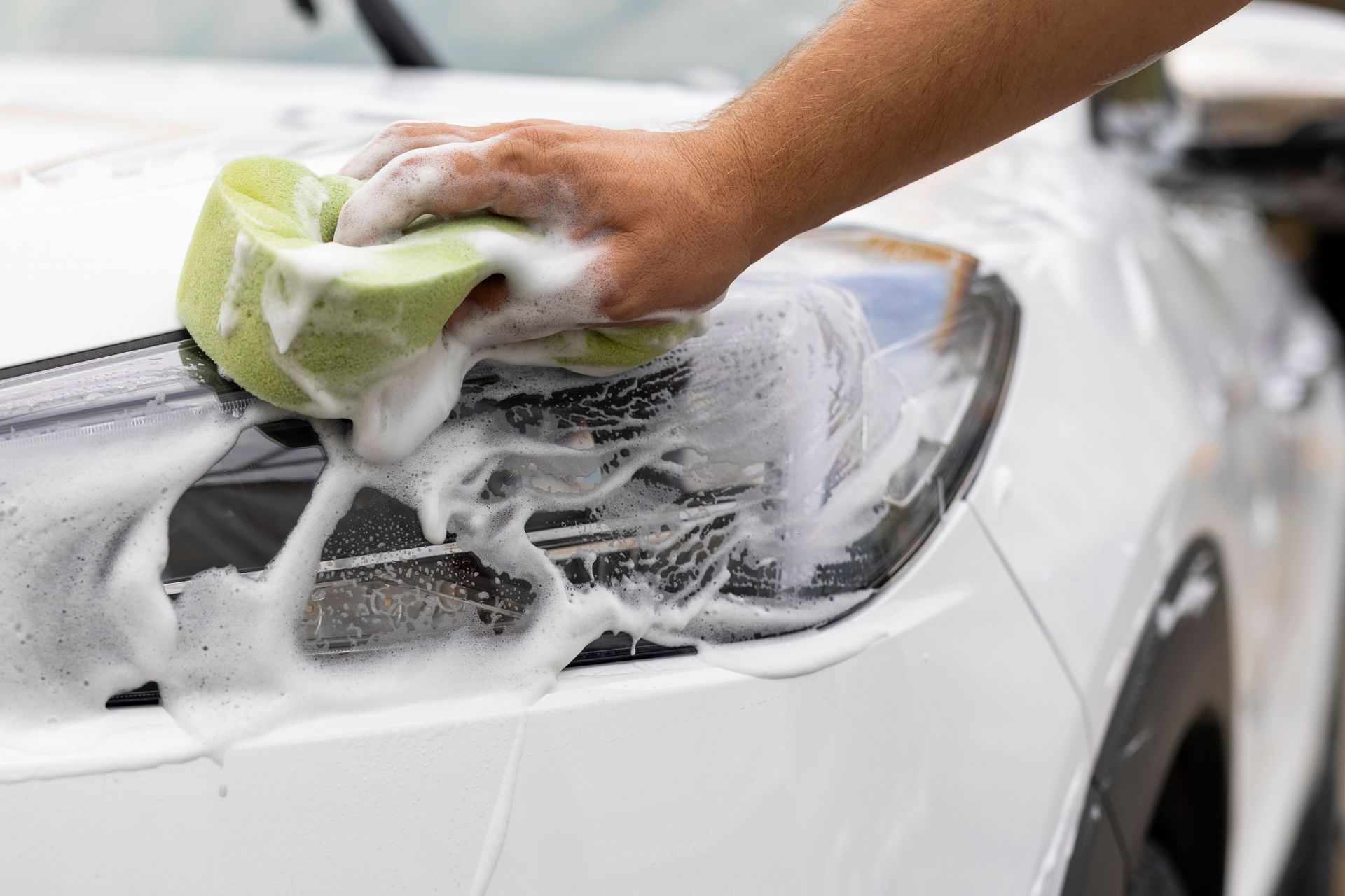 A person is washing a white car with a sponge.