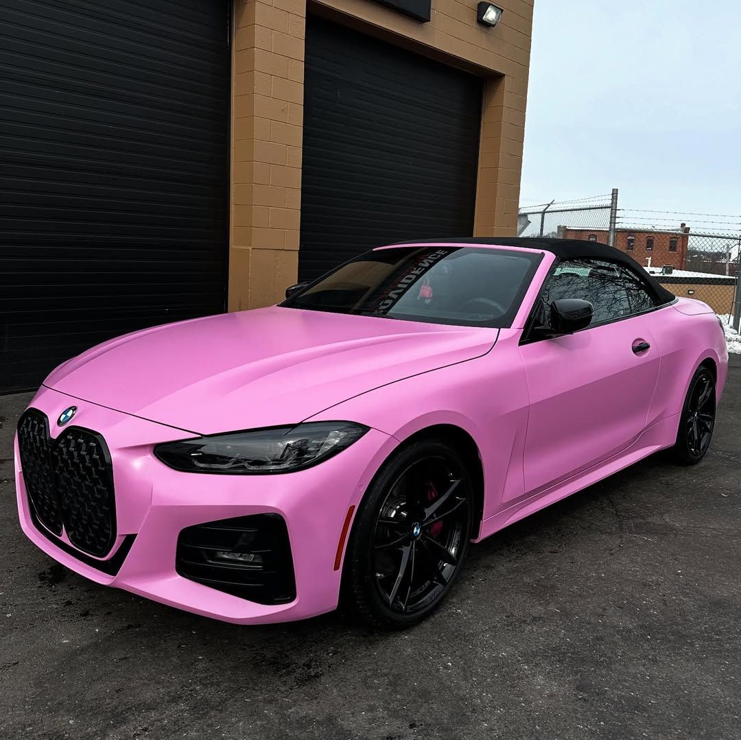 A pink bmw 4 series convertible is parked in front of a garage.