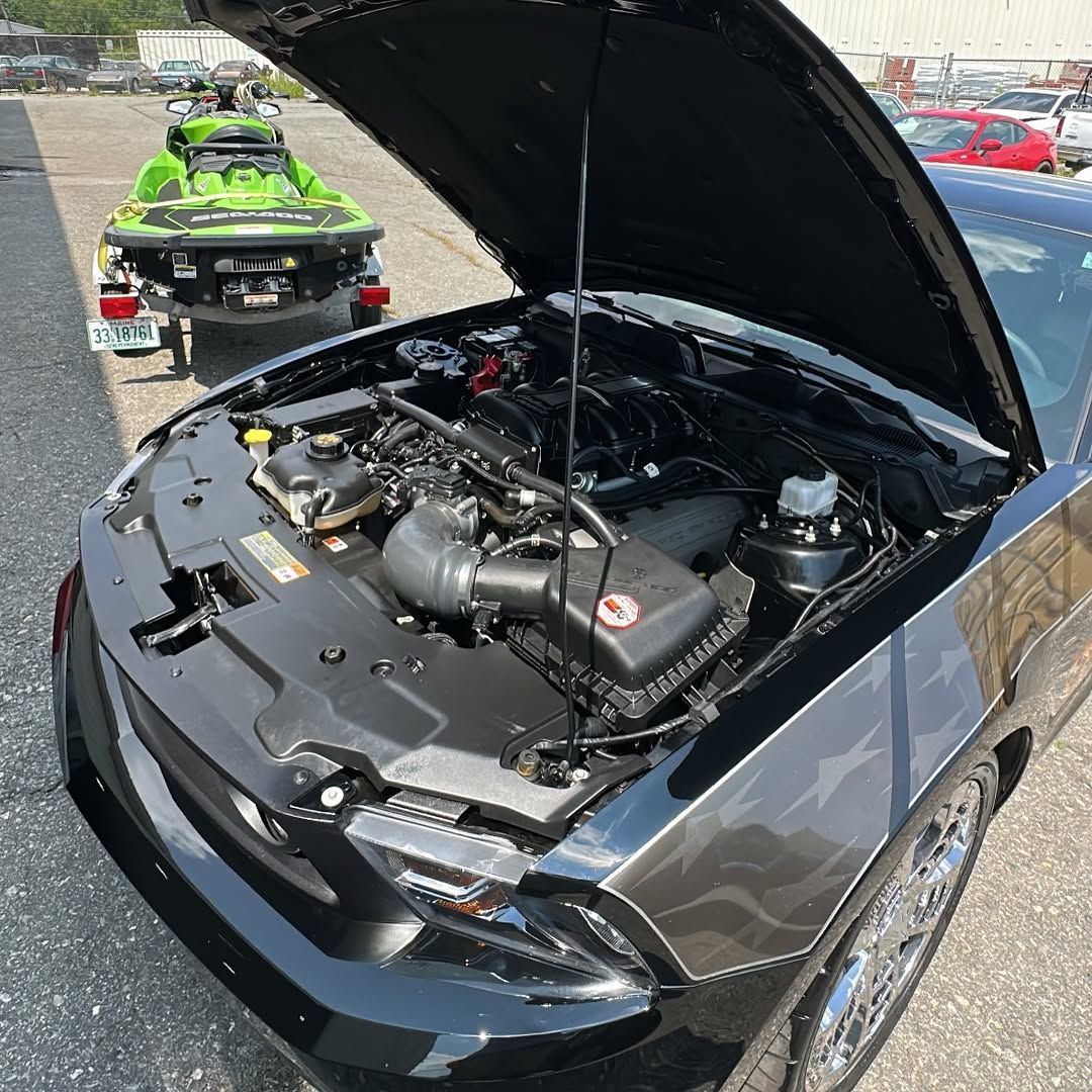 A black car with the hood open and a green jet ski in the background