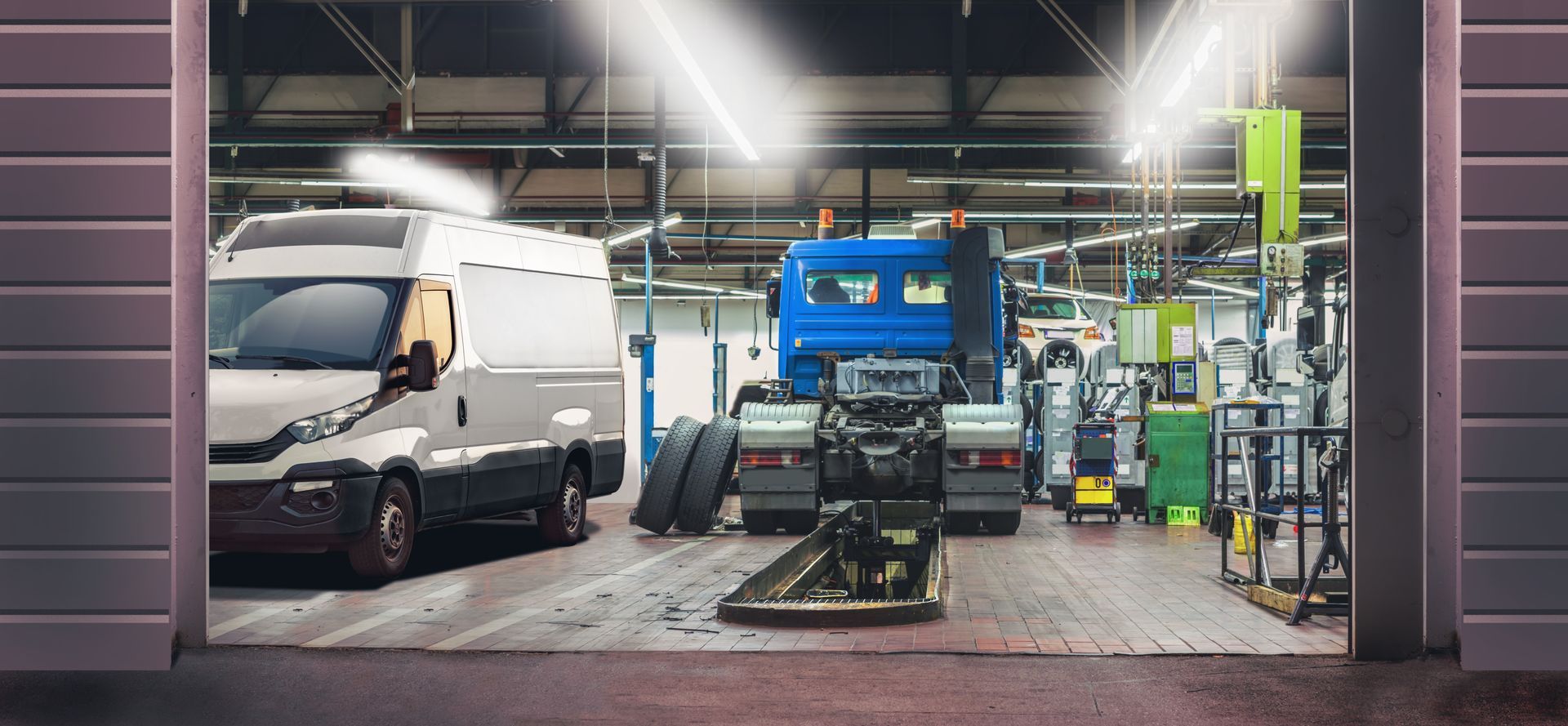 Truck repair shop with blue semi-truck and white van inside a brightly lit service bay.