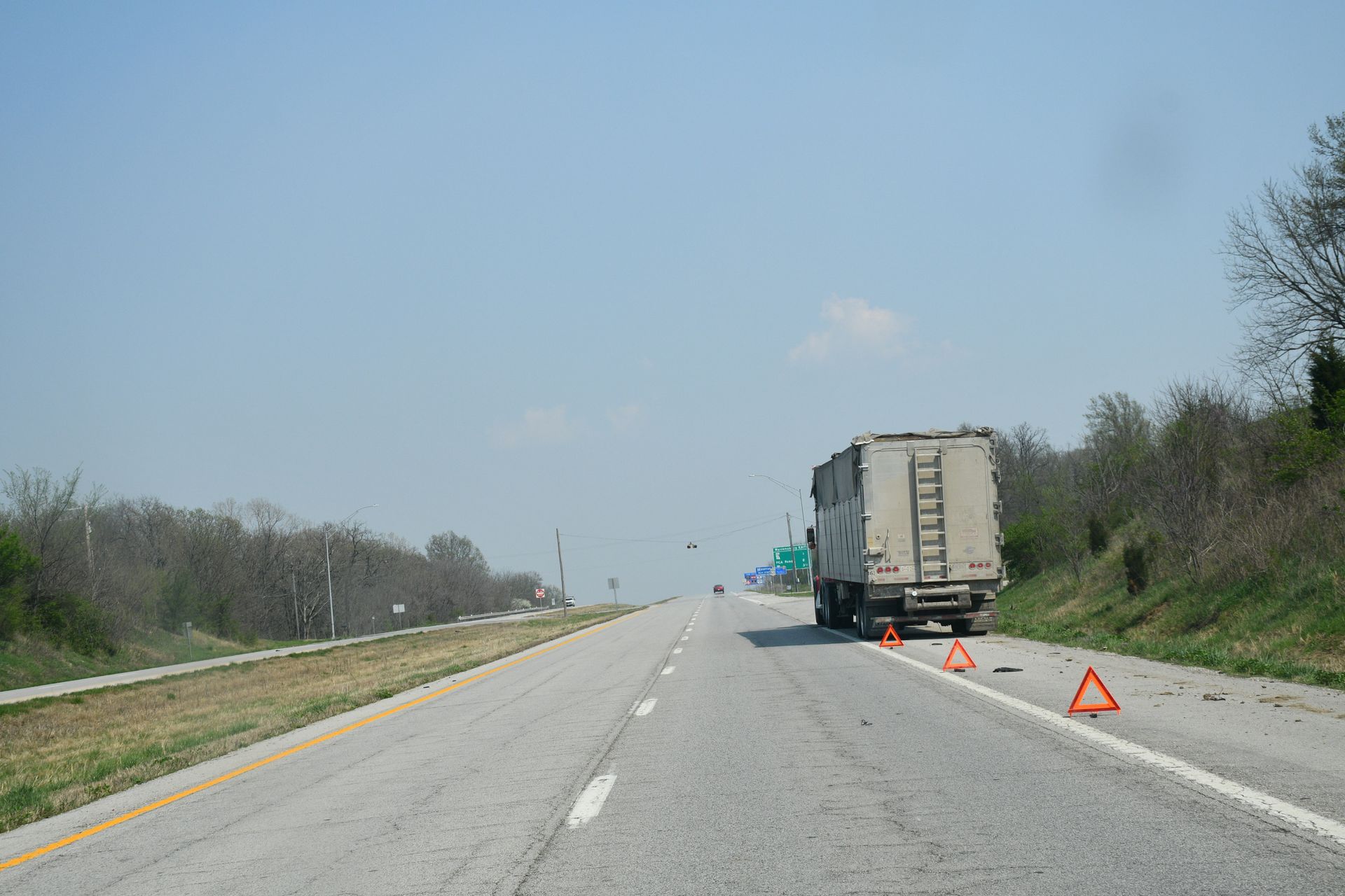 Disabled semi truck parked on highway shoulder with warning triangles set behind it.