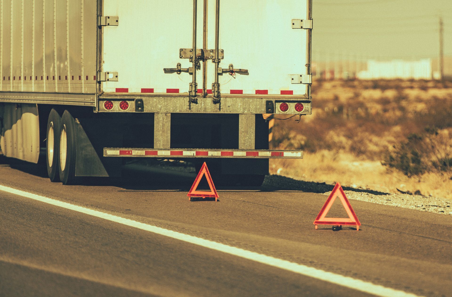 Truck stopped on roadside with two warning triangles placed behind for safety.
