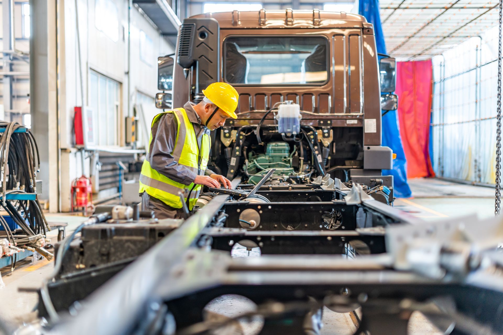 A factory worker is engaged in truck repair, using tools to fix a vehicle in a busy workshop. A factory worker is engaged in truck repair, using tools to fix a vehicle in a busy workshop.