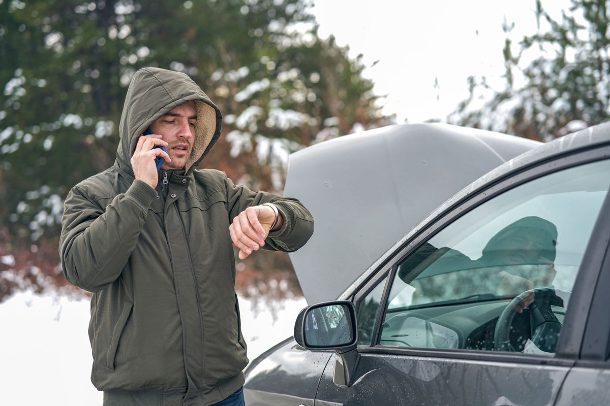 A man looks at his watch, waiting for roadside assistance.