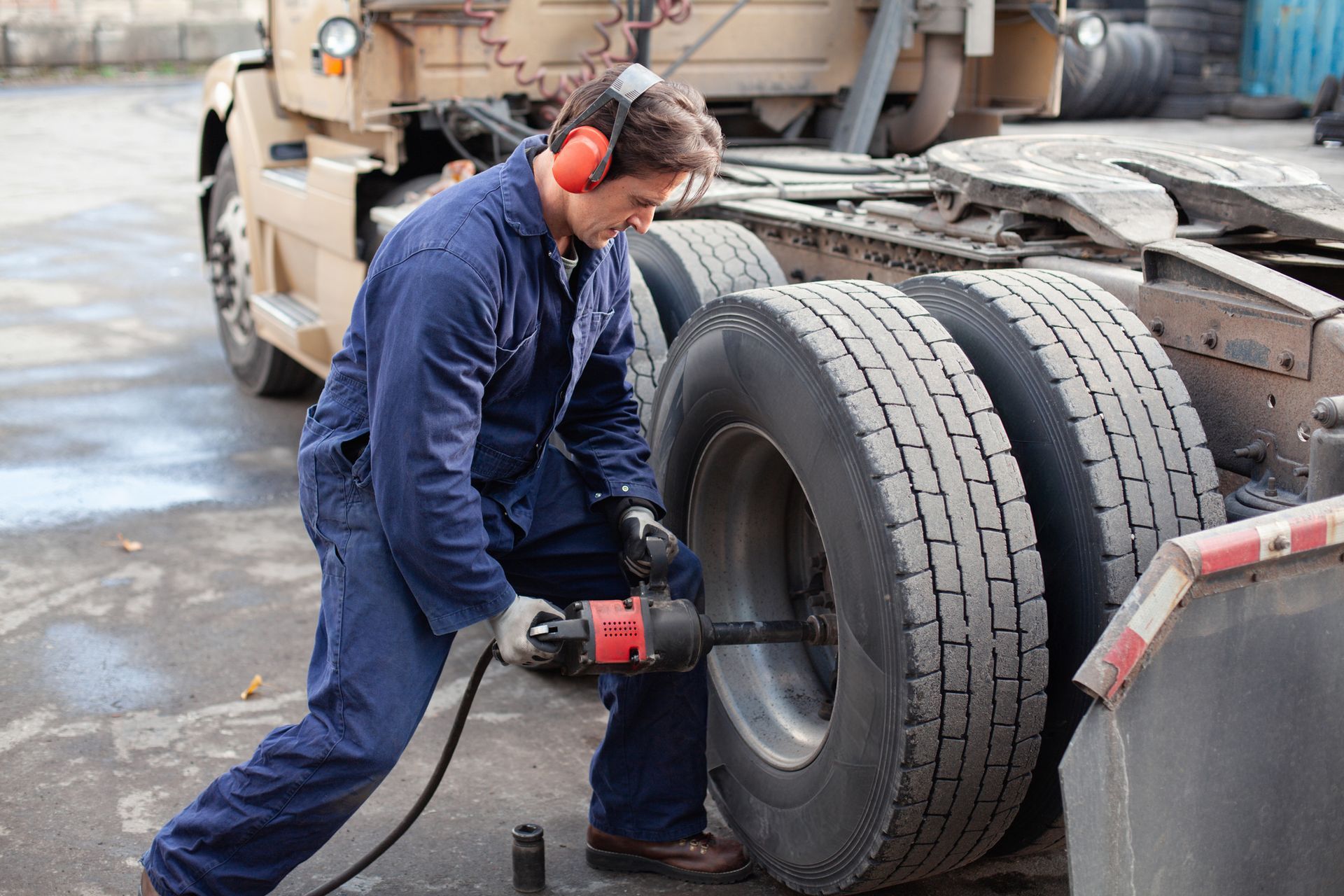 A mechanic using power tools in an auto garage is performing truck repair service on a vehicle. A mechanic using power tools in an auto garage is performing truck repair service on a vehicle.