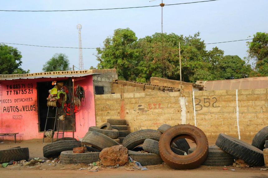 A tire repair shop with a pink facade and a pile of discarded tires in the foreground against a block wall.