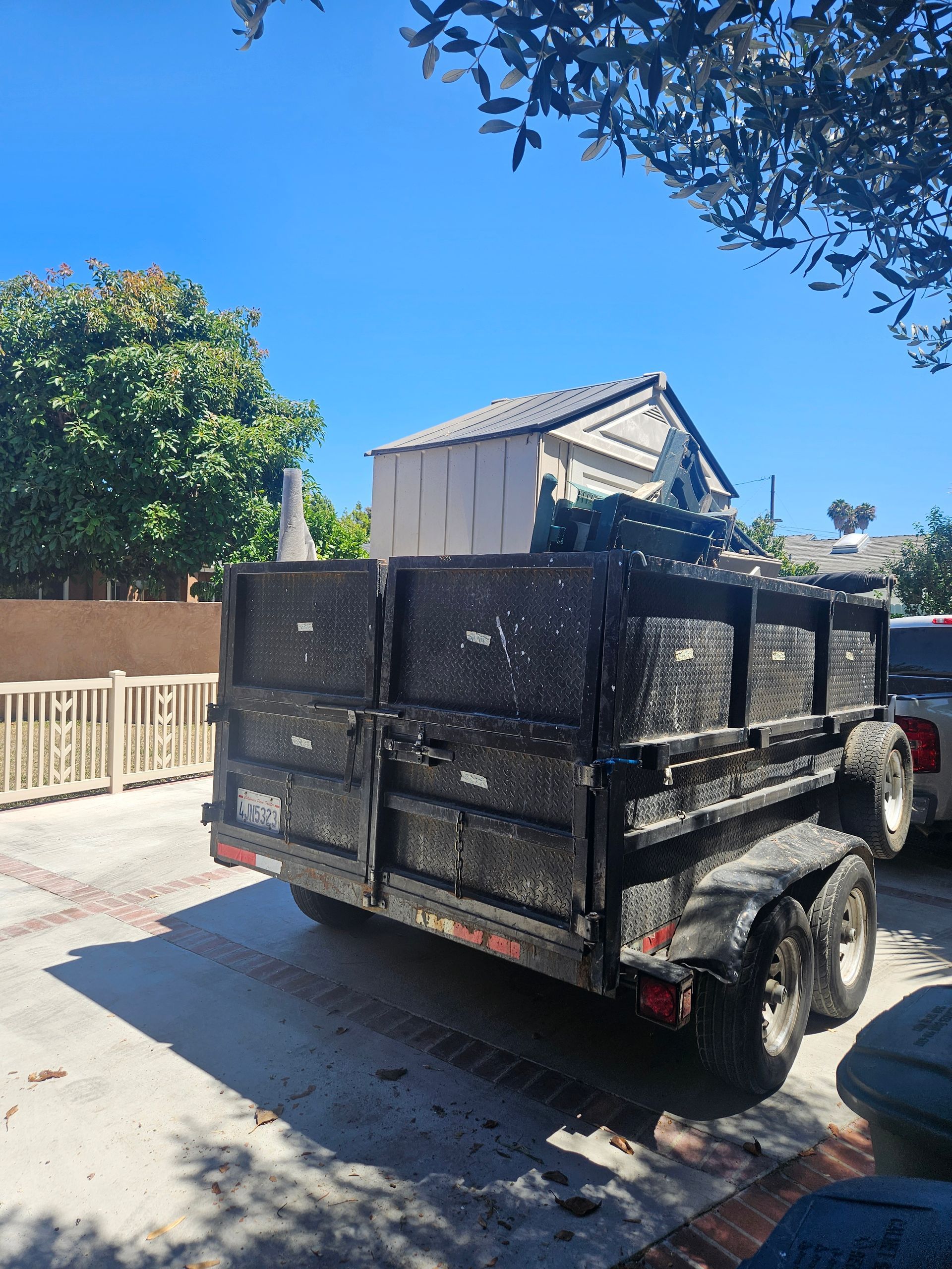 A white moving truck parked on a residential street next to boxes and trash bins, with palm trees and houses nearby.