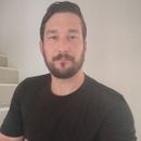 Man with dark hair and beard, wearing a black shirt, looking towards the camera.