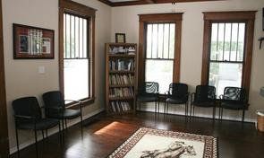 A waiting room with chairs , a rug and a bookshelf.