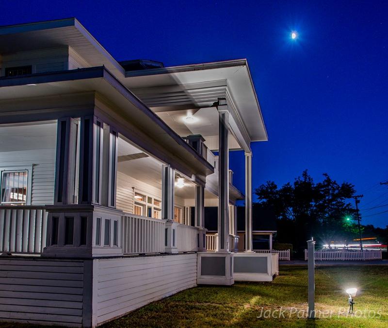 A white house is lit up at night with a full moon in the sky