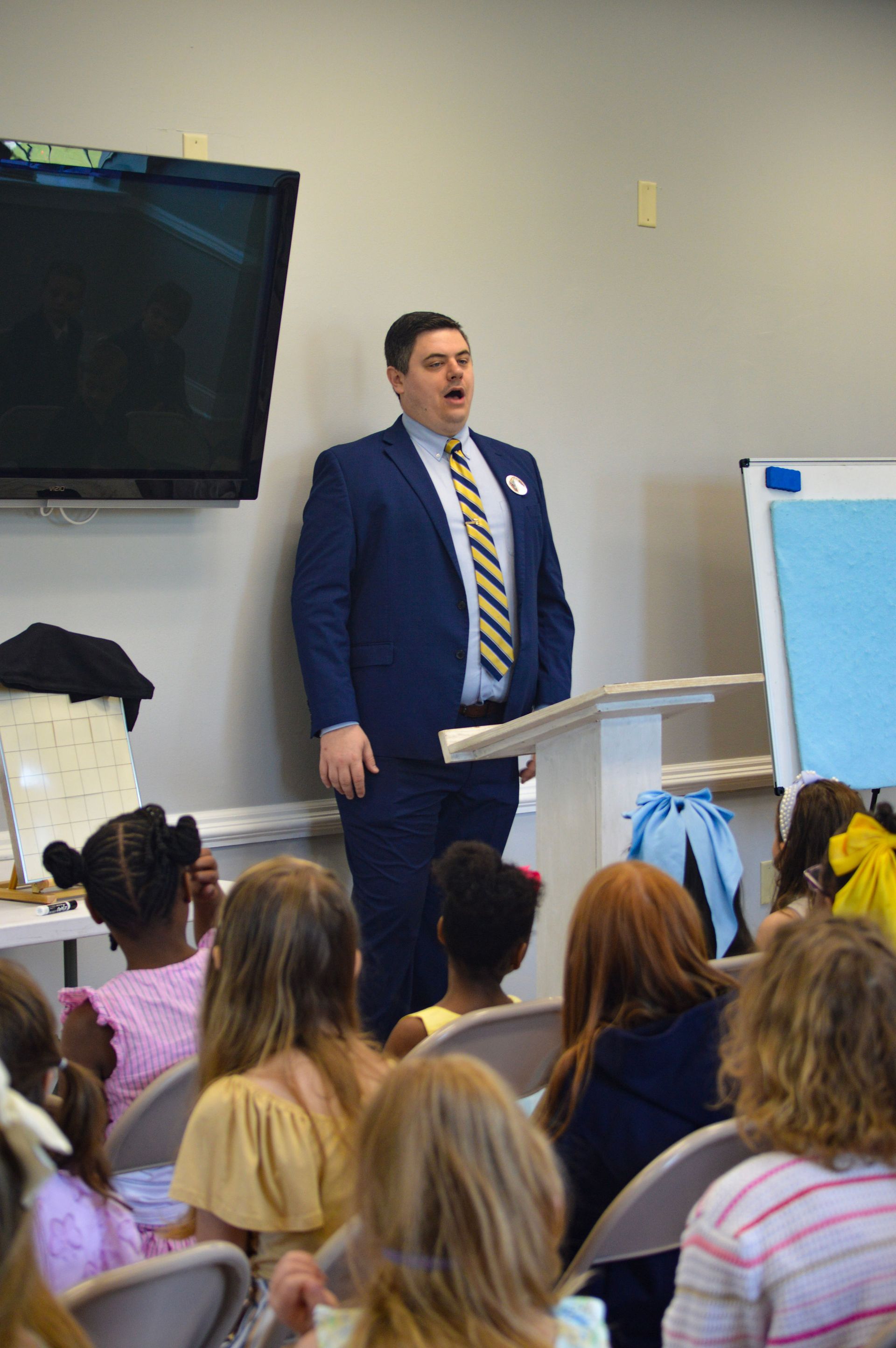 Man leading children in pledge, holding a Christian flag in a classroom setting.