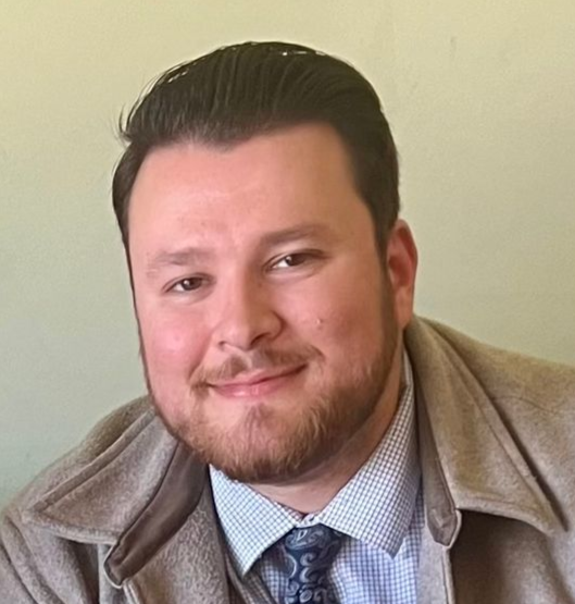 Man in a suit and glasses smiles at the camera.