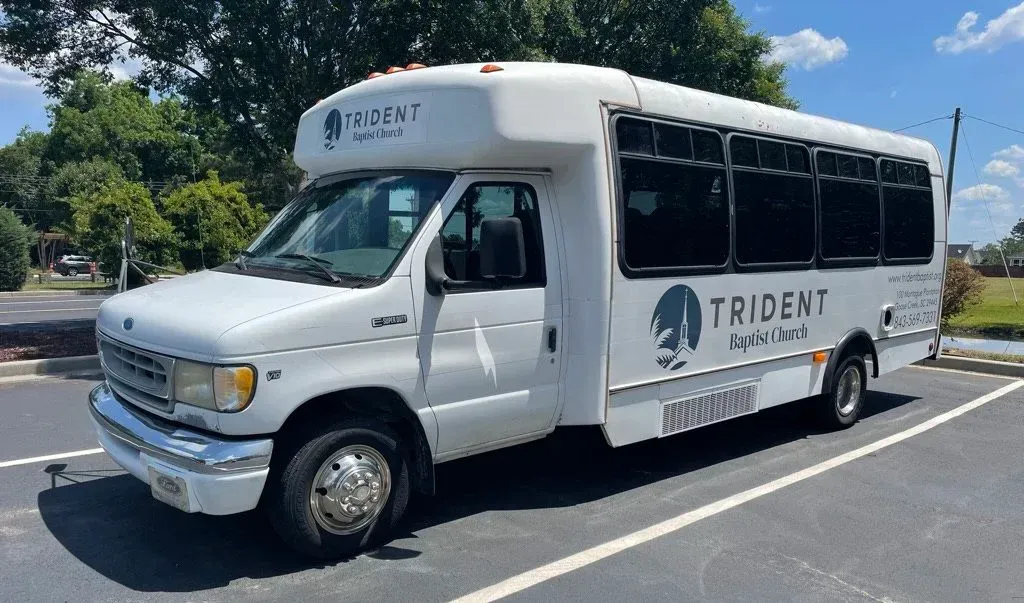 A white transit bus with the Trident Baptist Church logo on it