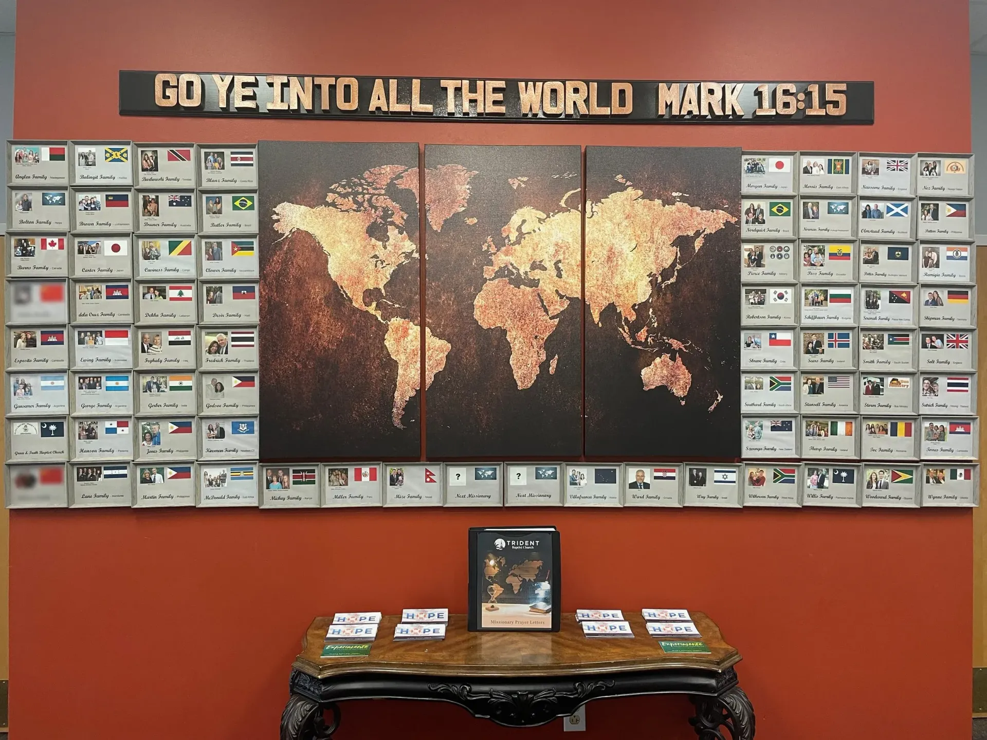 A wall display with a world map, flags, and a biblical verse.