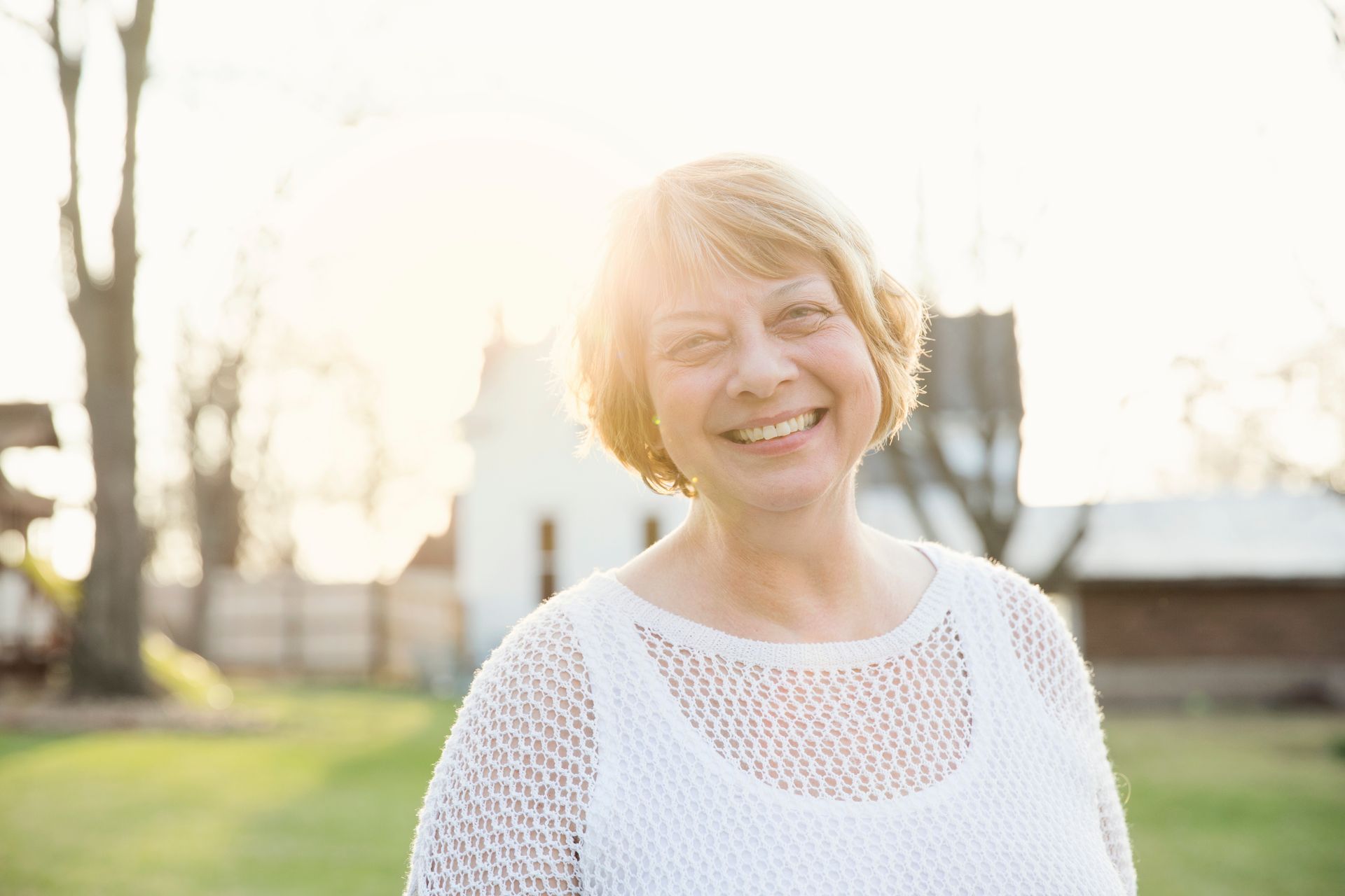 Woman with blonde hair smiles in sunny backyard.