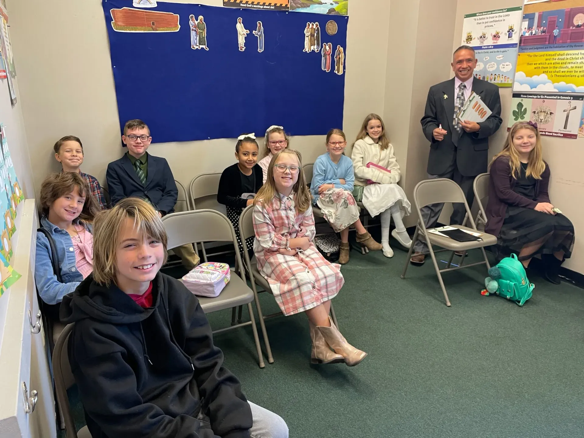 A group of children and a man in suits sit in a room, possibly at a gathering.