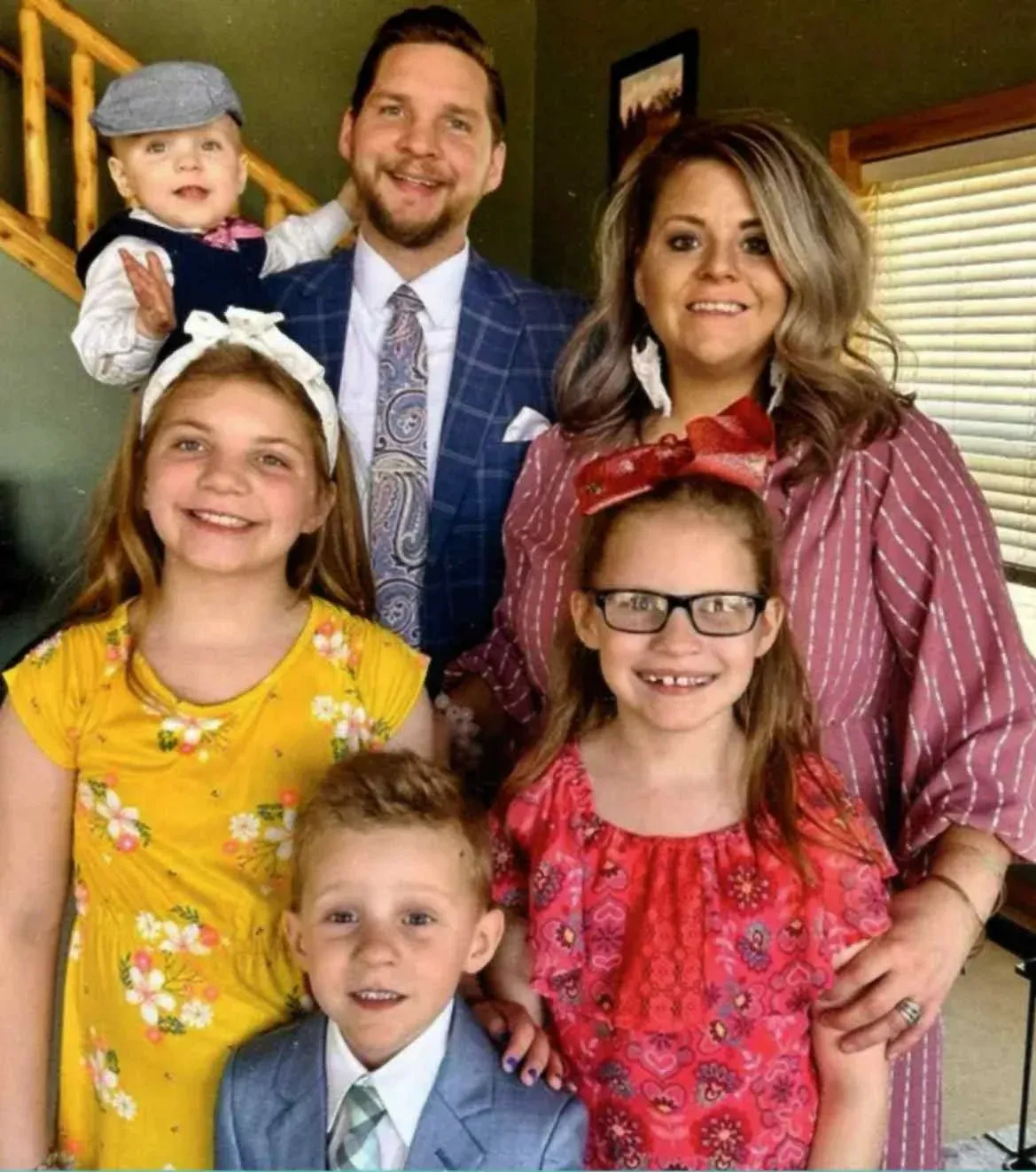 Family of six smiling for the camera. Includes a baby, two young girls, a young boy, and parents in a home.
