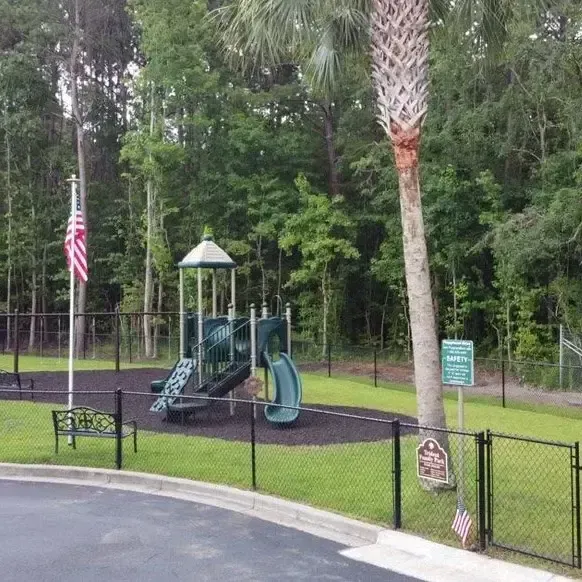 Playground with green equipment, black fence, American flag, and palm tree.
