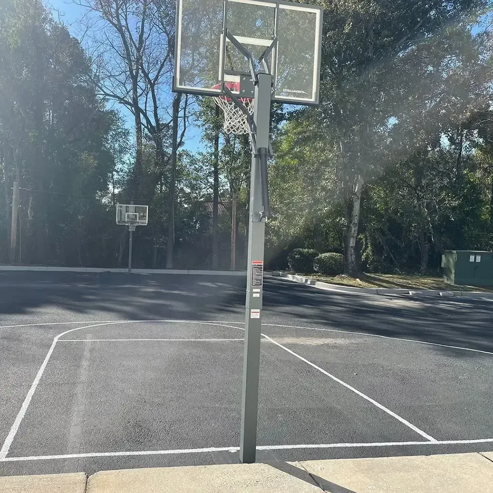 Basketball court with two hoops, trees in the background, and a sunny day.