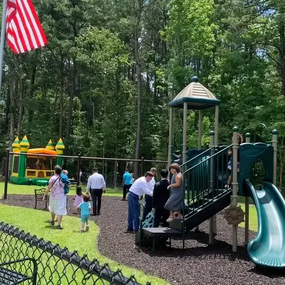 People at a playground with a slide, inflatable bouncer, and US flag.