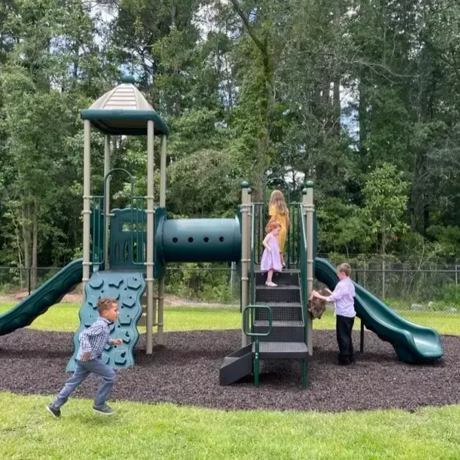 Children playing on a green playground with slides, climbing wall, and tunnel in a park.