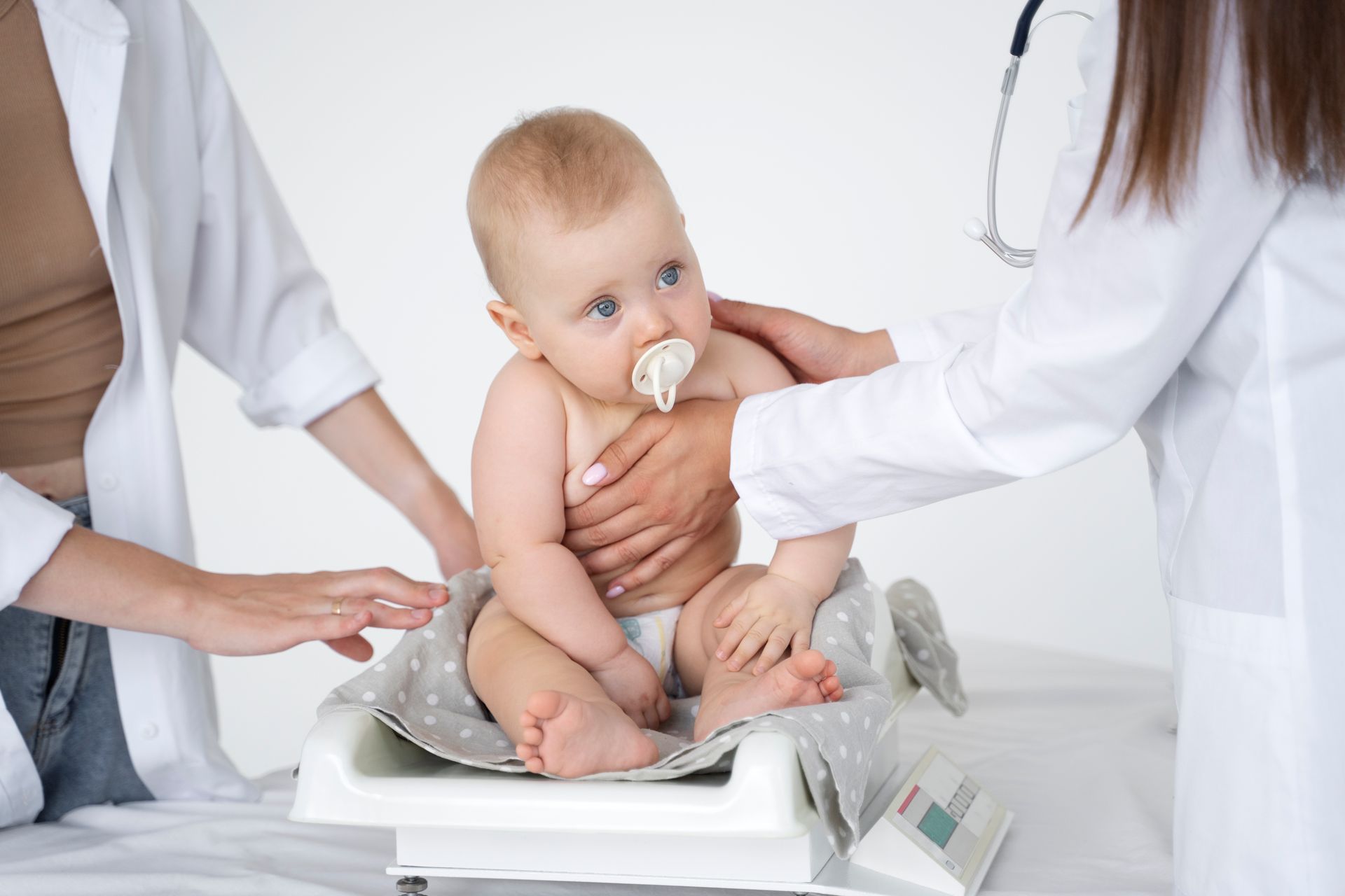 Un bebé está sentado en una báscula con un chupete en la boca.