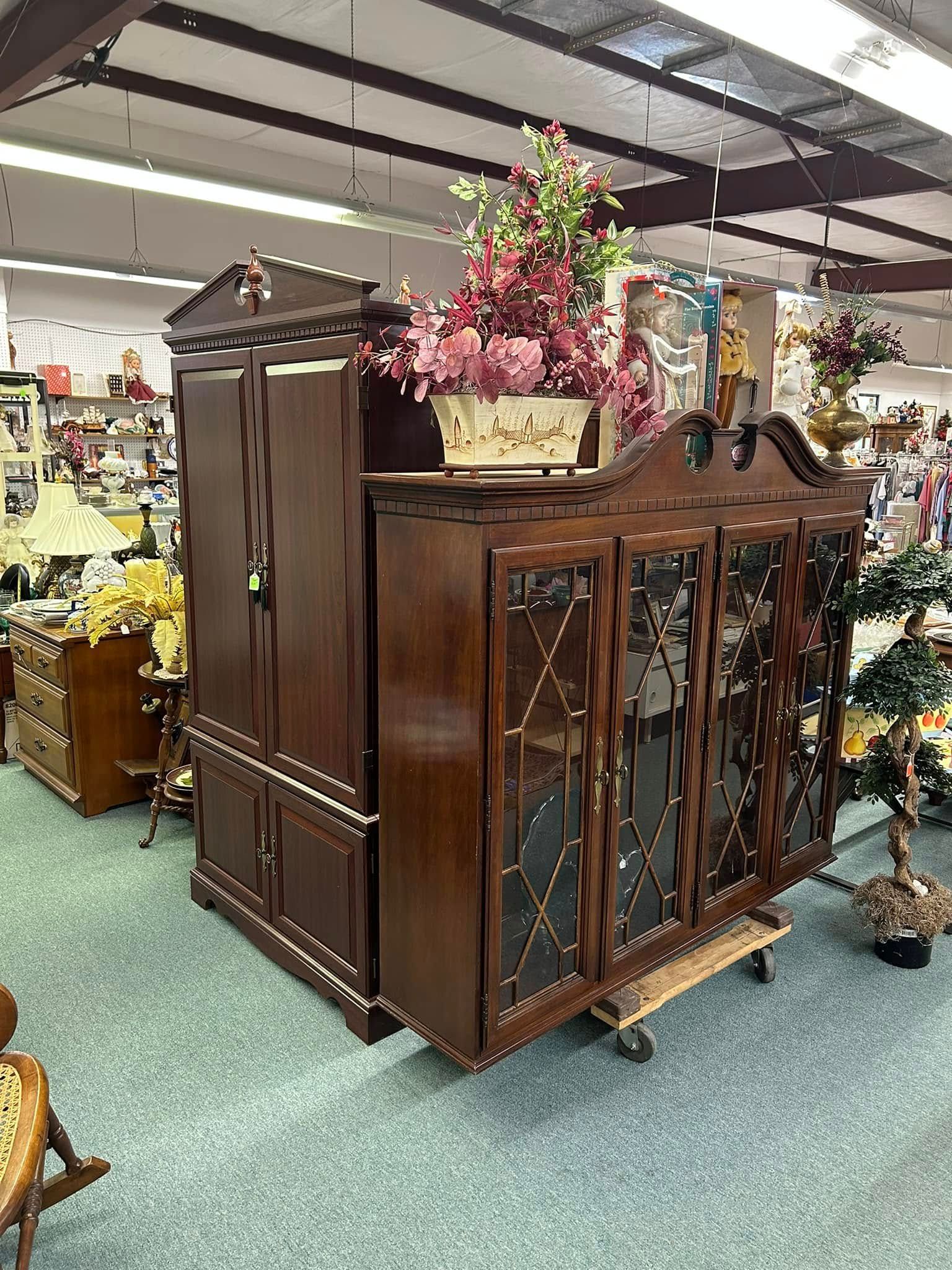 Dark wooden antique cabinet with flowers on top in a showroom aisle