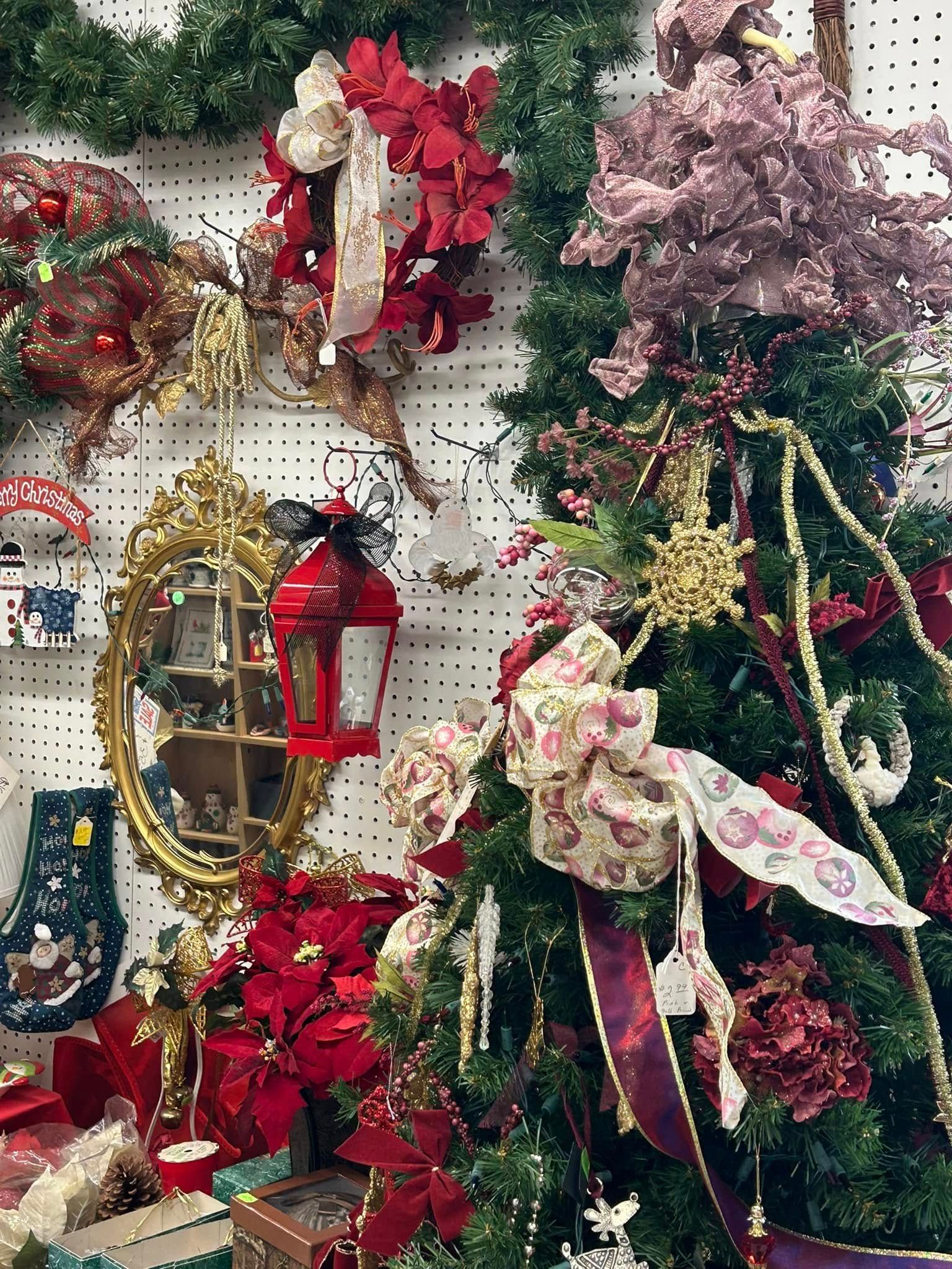 Holiday décor display with red, gold, and pink ornaments, wreaths, and a decorated Christmas tree on a pegboard wall
