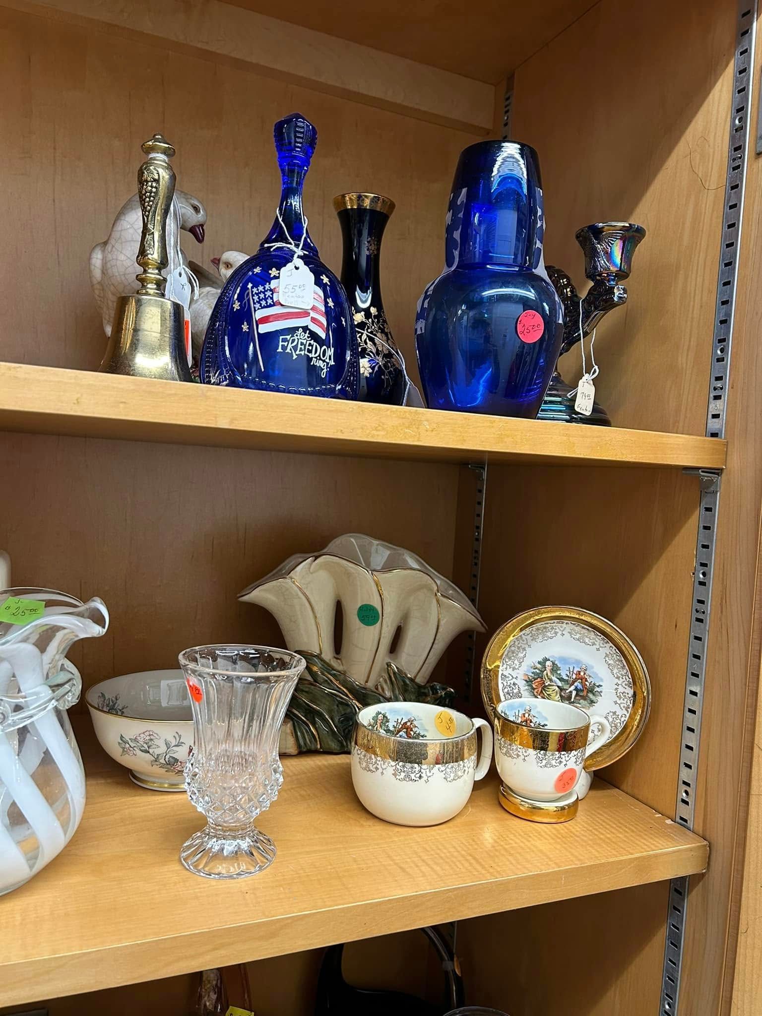Shelf with assorted glassware and figurines, including blue vases and decorative cups on a wooden cabinet.