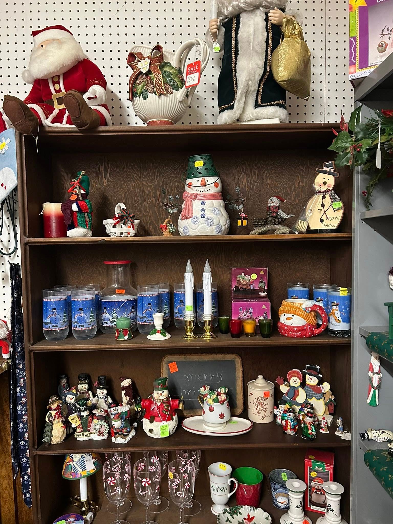 Wooden shelf filled with colorful Christmas figurines, candles, and holiday decorations