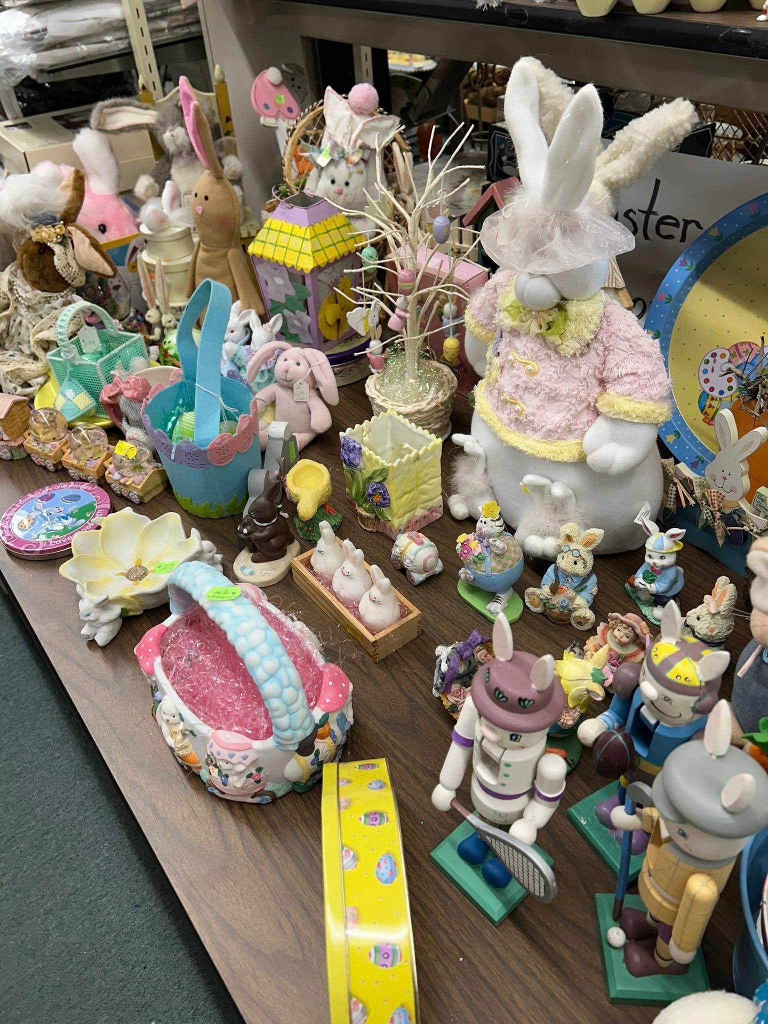 Table display of pastel Easter bunny figurines, chicks, and spring decorations in a store or market.