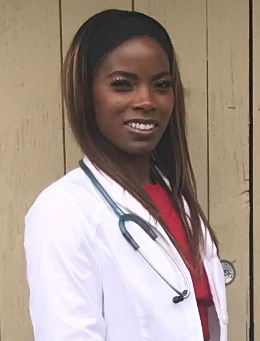 Black woman in white coat with stethoscope, smiling.