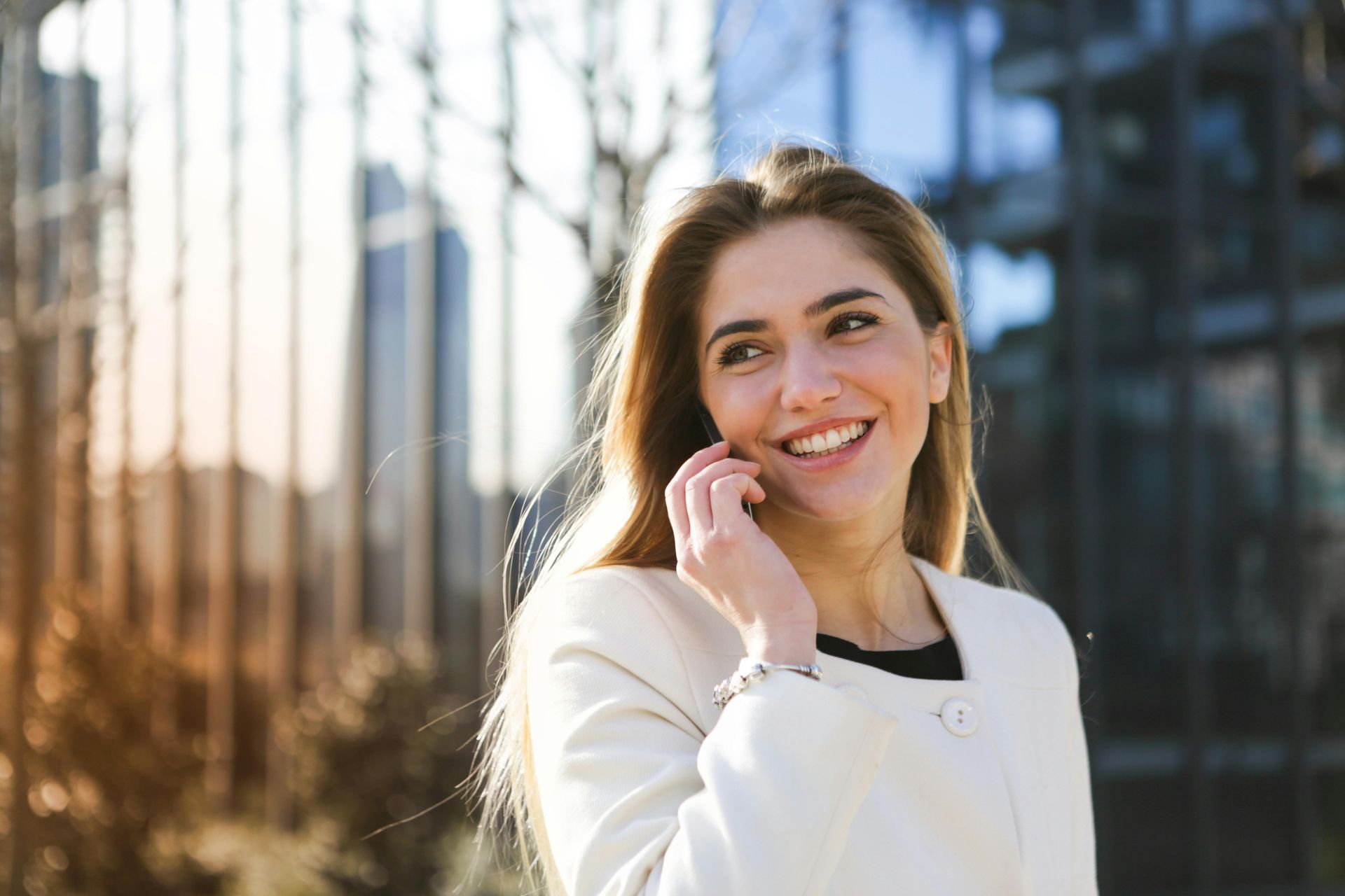 Woman smiling, holding tablet, talking on phone outside a building.