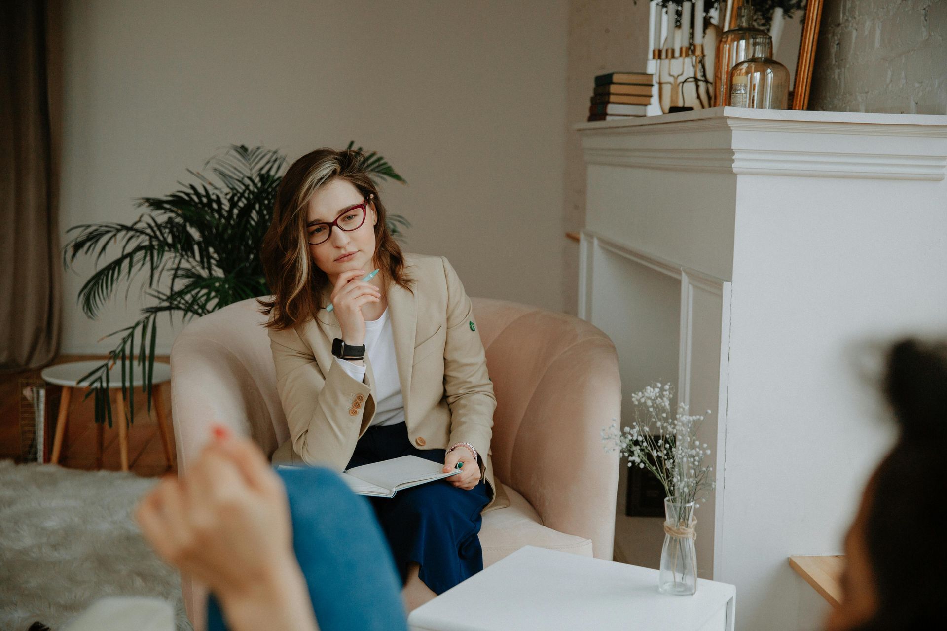 Woman therapist in glasses listens thoughtfully to patient in an armchair.