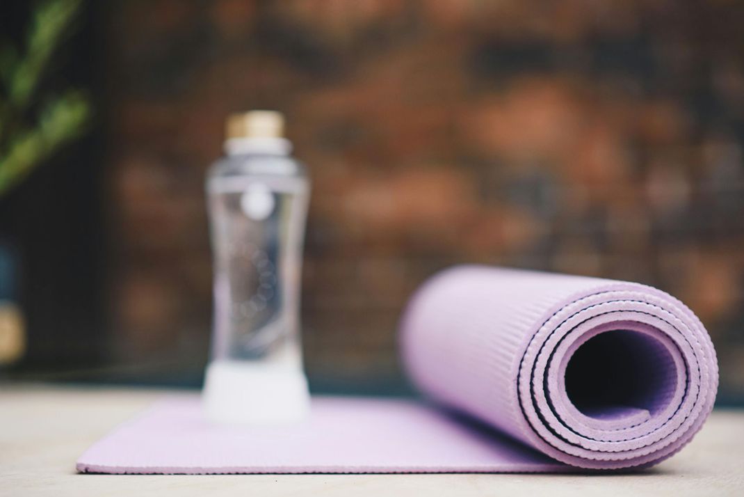 Rolled lavender yoga mat and water bottle on a wooden surface.